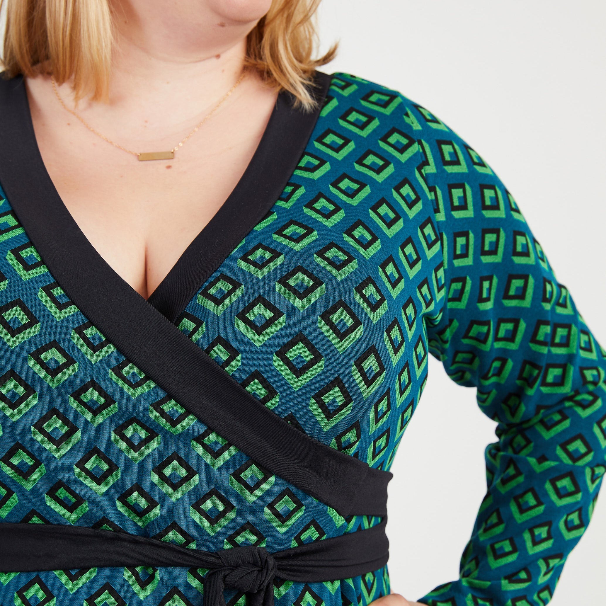 Woman wearing a green and black patterned dress with a black belt. This dress is the Appleton Wrap Dress sewing pattern from Cashmerette.