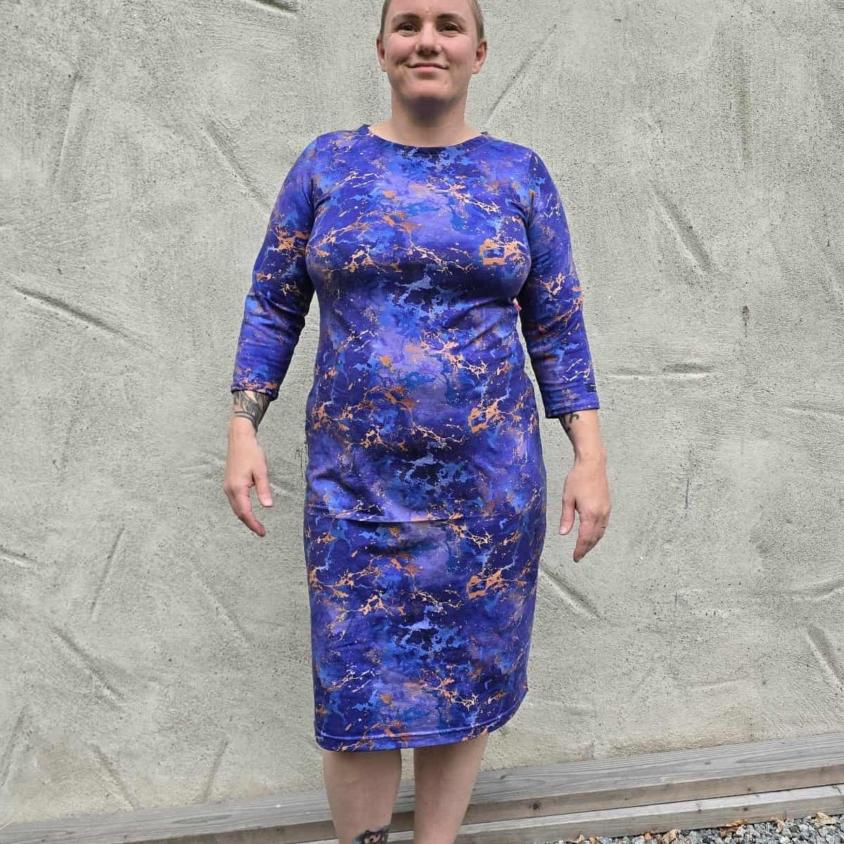 Person wearing a blue floral dress standing against a textured gray wall.