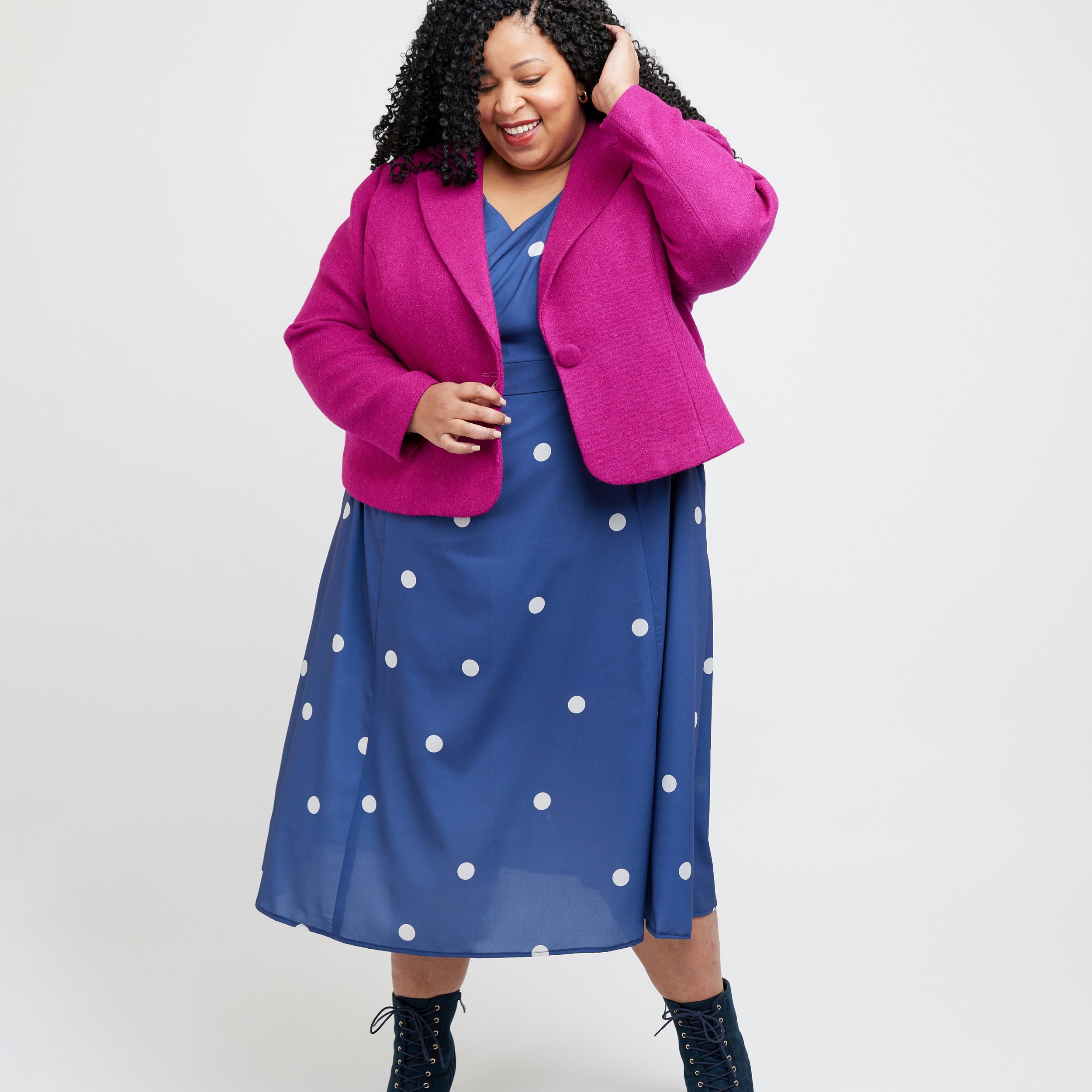 Woman wearing a bright pink coat over a blue dress with white polka dots on a white background. This blazer is the Auburn Blazer sewing pattern from Cashmerette.