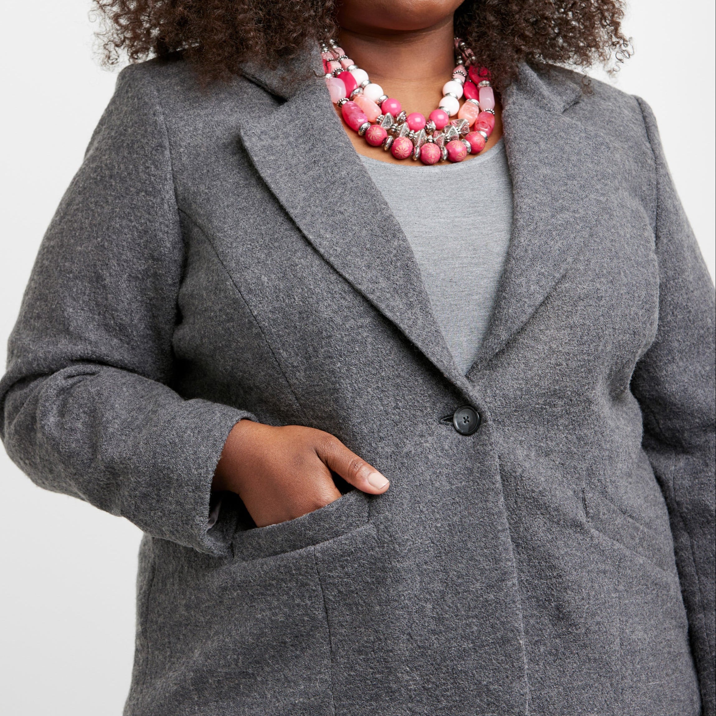 Woman wearing a gray blazer over a gray top with a pink necklace on a white background. This blazer is the Auburn Blazer sewing pattern from Cashmerette.