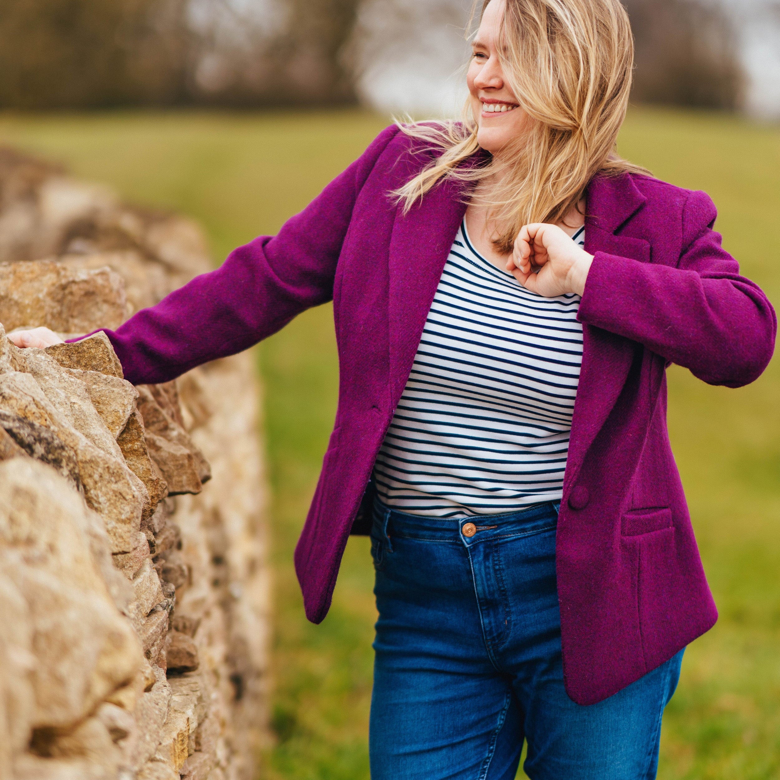 Woman in a purple coat standing next to a stone wall in a field. This blazer is the Auburn Blazer sewing pattern from Cashmerette.