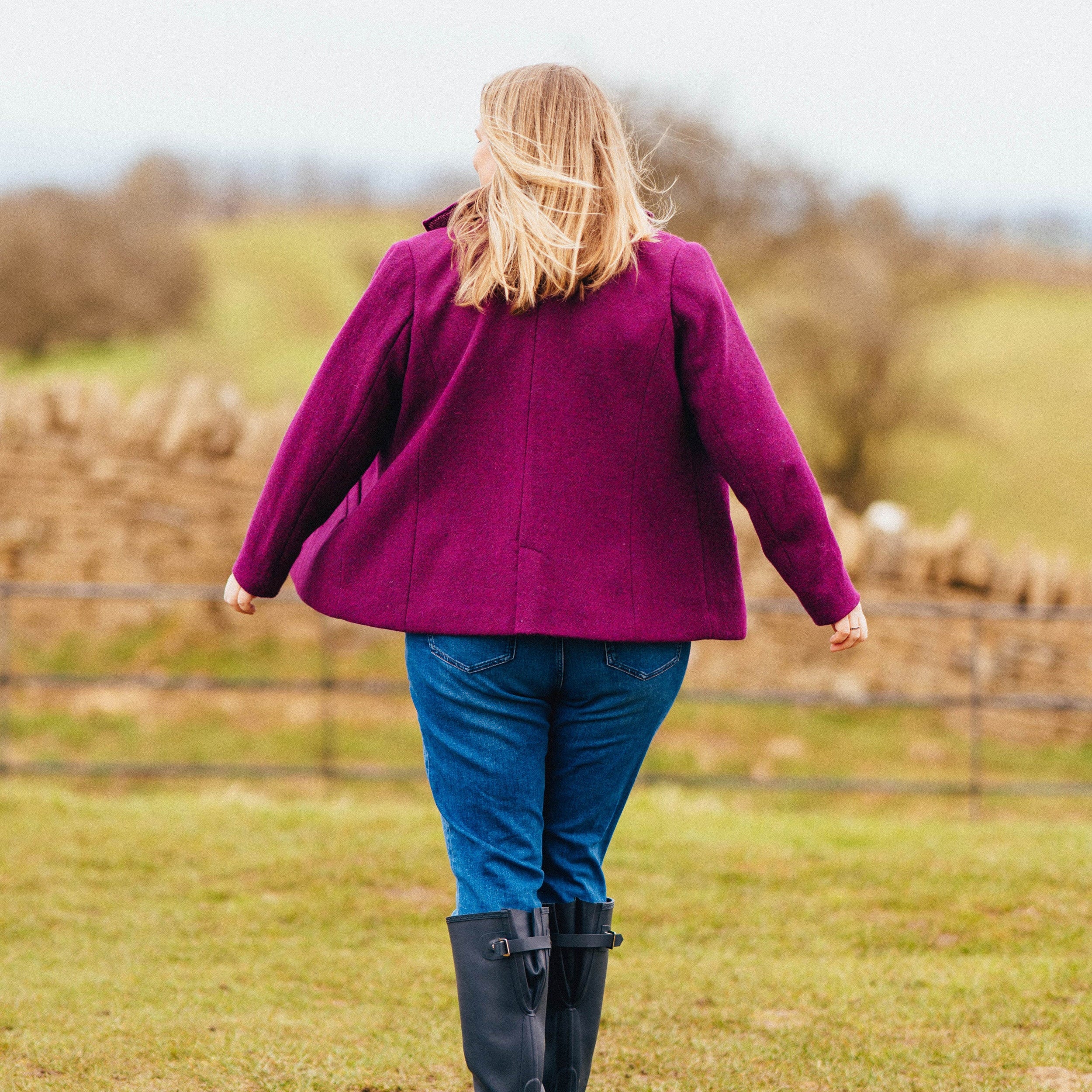 Person wearing a purple coat and blue jeans standing in a field. This blazer is the Auburn Blazer sewing pattern from Cashmerette.