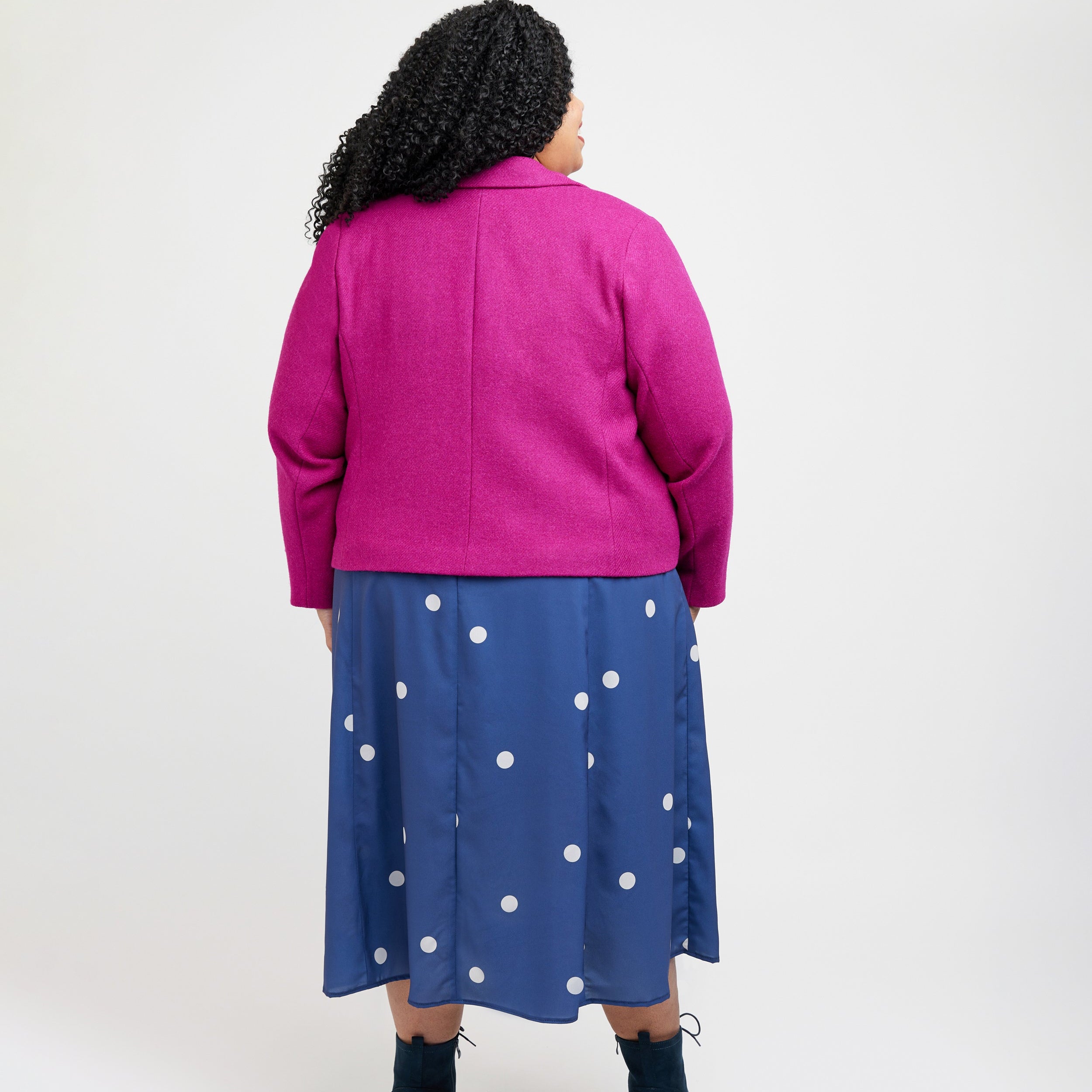 Person wearing a pink jacket and blue polka dot dress on a white background. This blazer is the Auburn Blazer sewing pattern from Cashmerette.