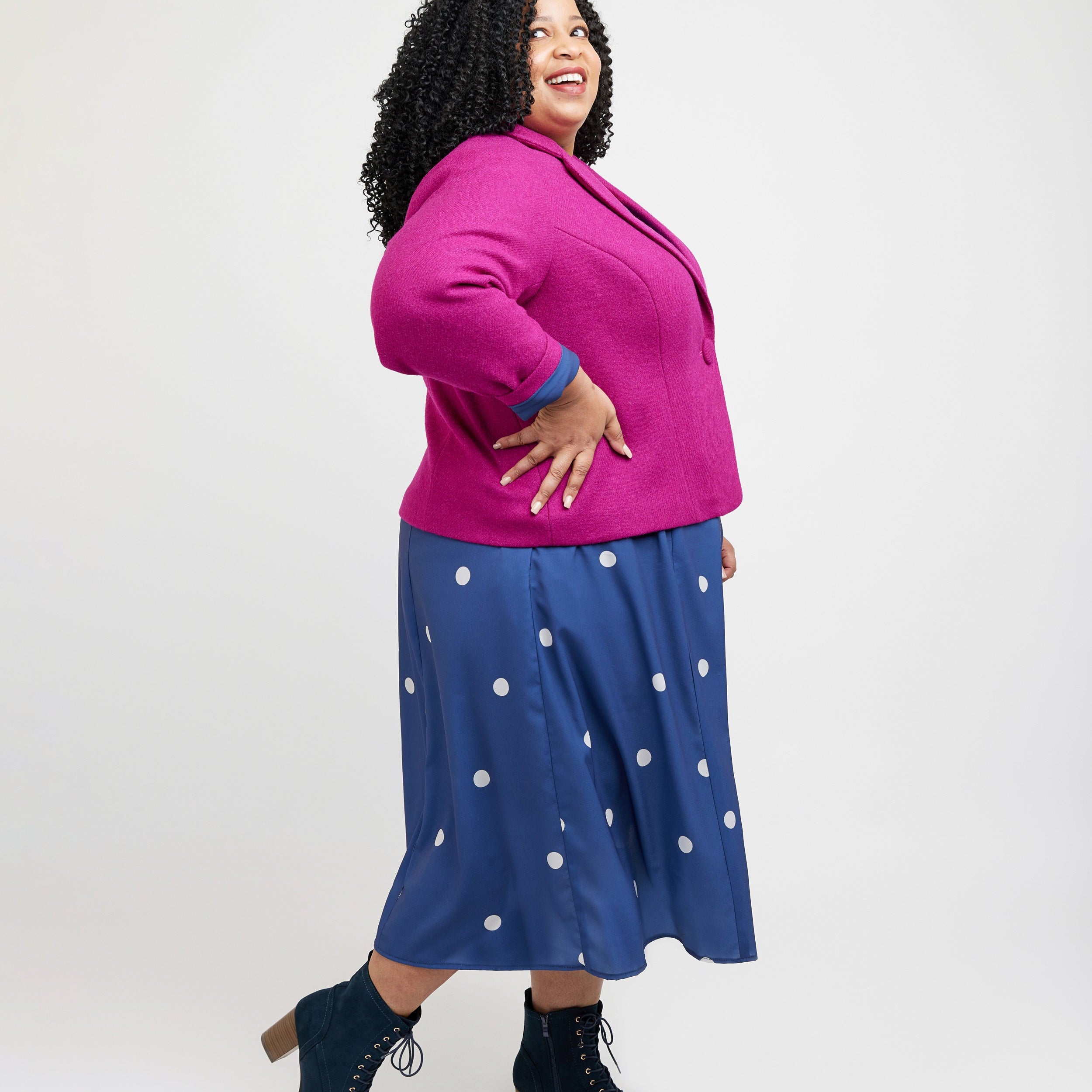 Woman wearing a pink jacket and blue polka dot skirt on a white background. This blazer is the Auburn Blazer sewing pattern from Cashmerette.