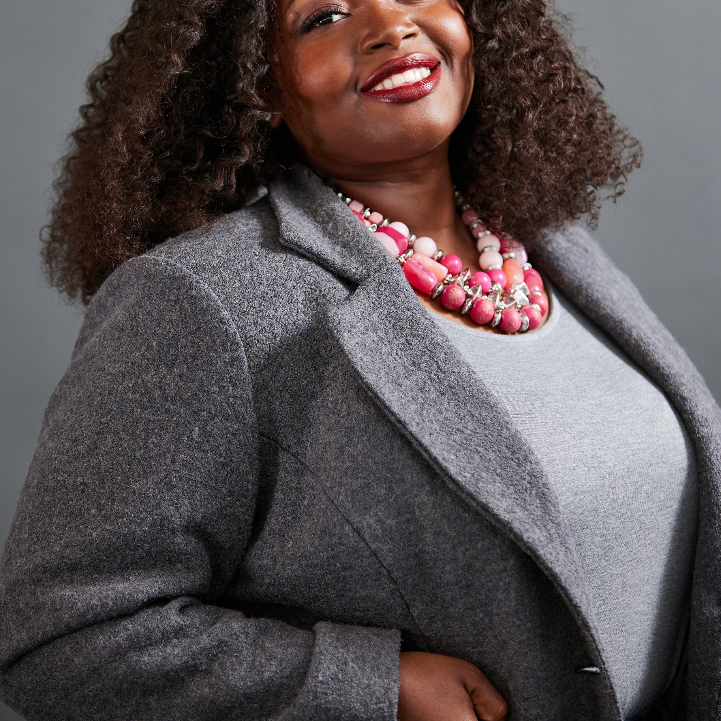 Woman wearing a gray coat and pink necklace against a gray background. This blazer is the Auburn Blazer sewing pattern from Cashmerette.