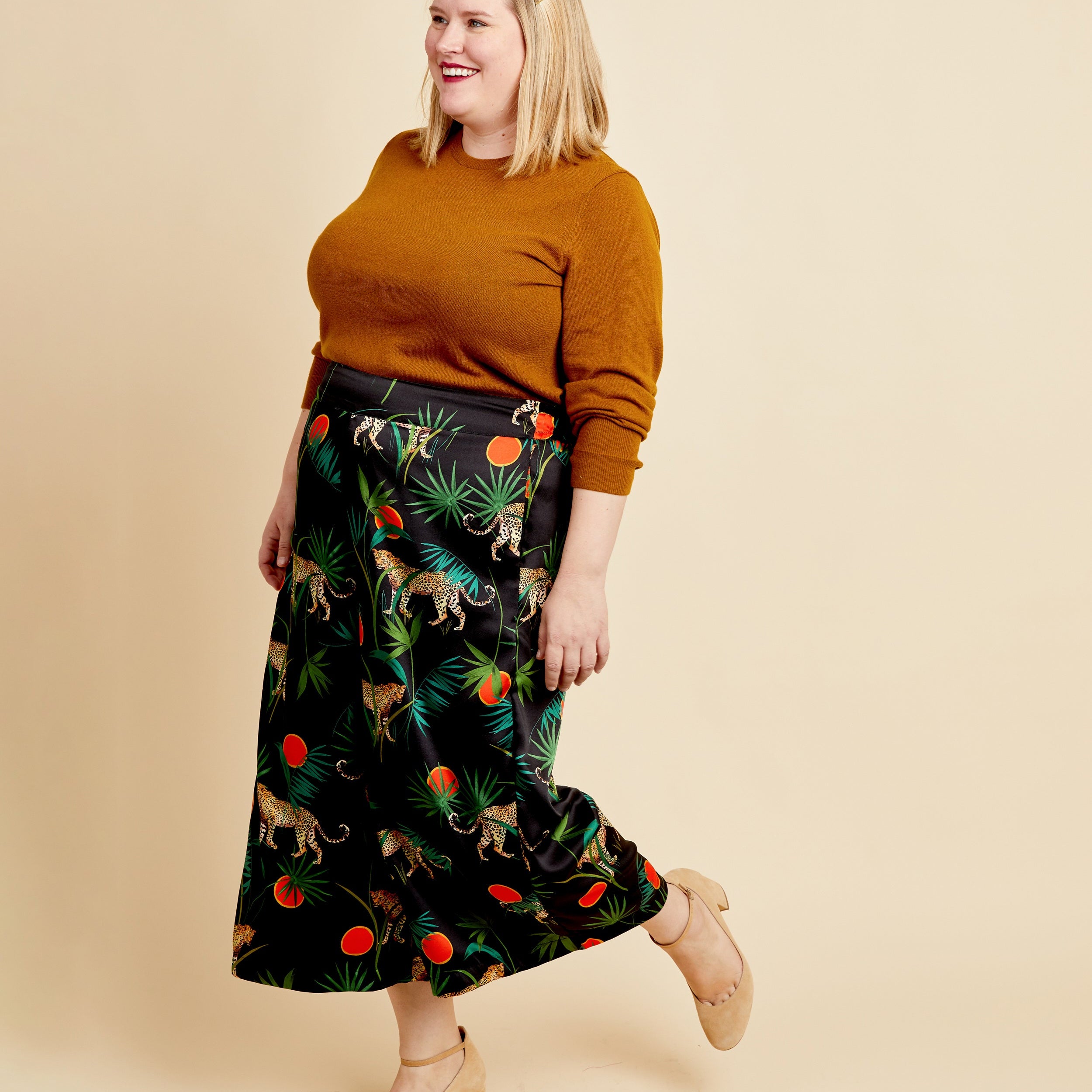 Woman wearing a mustard sweater and patterned skirt on a beige background. These pants are the Calder Pants & Shorts sewing pattern from Cashmerette.