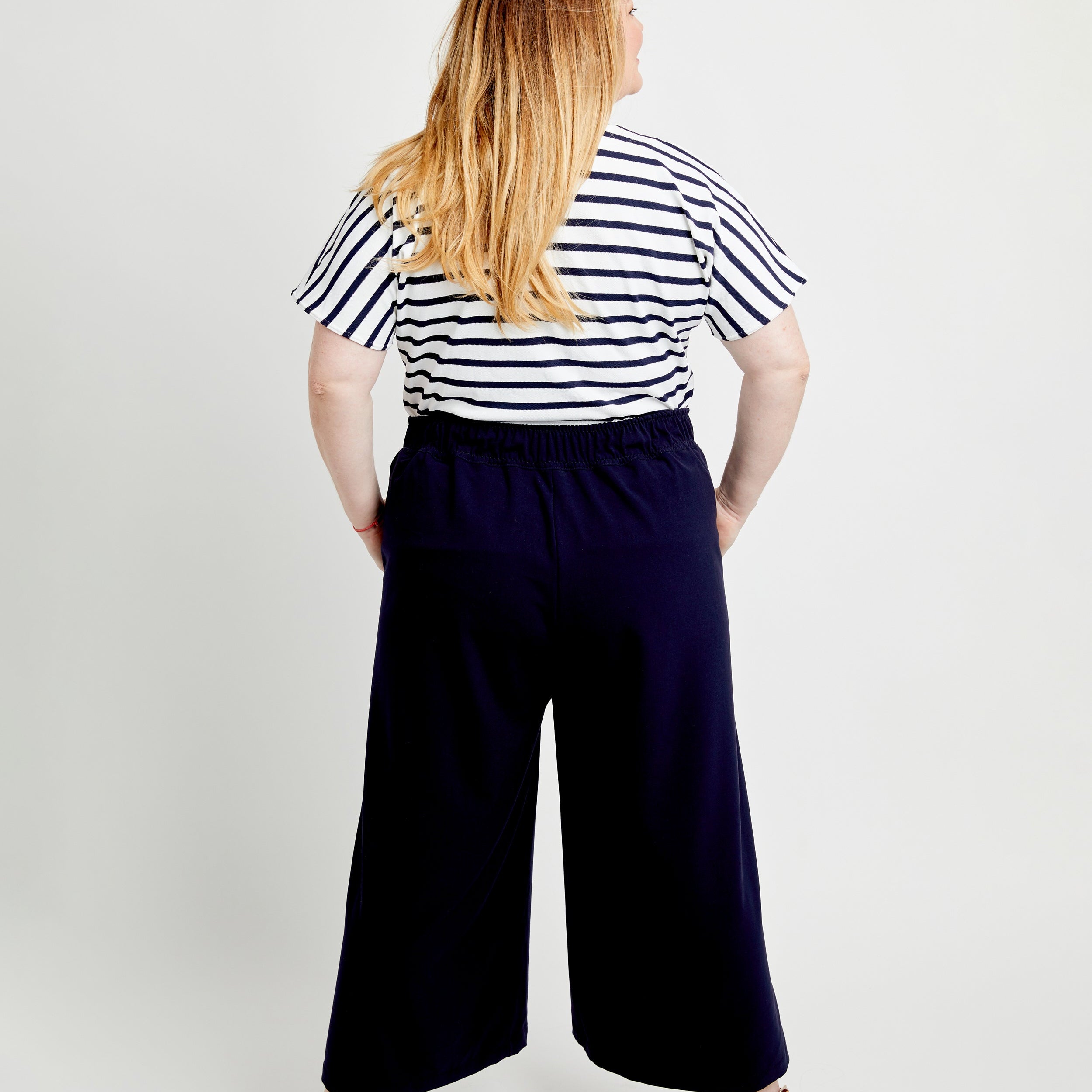 Person wearing a striped shirt and wide-leg pants on a white background. These pants are the Calder Pants & Shorts sewing pattern from Cashmerette.