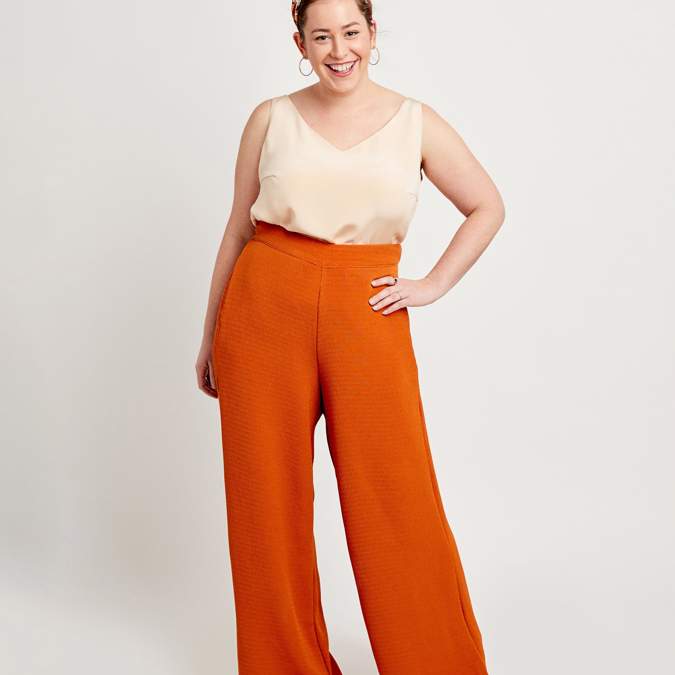 Woman wearing a cream top and orange wide-leg pants on a white background. These pants are the Calder Pants & Shorts sewing pattern from Cashmerette.