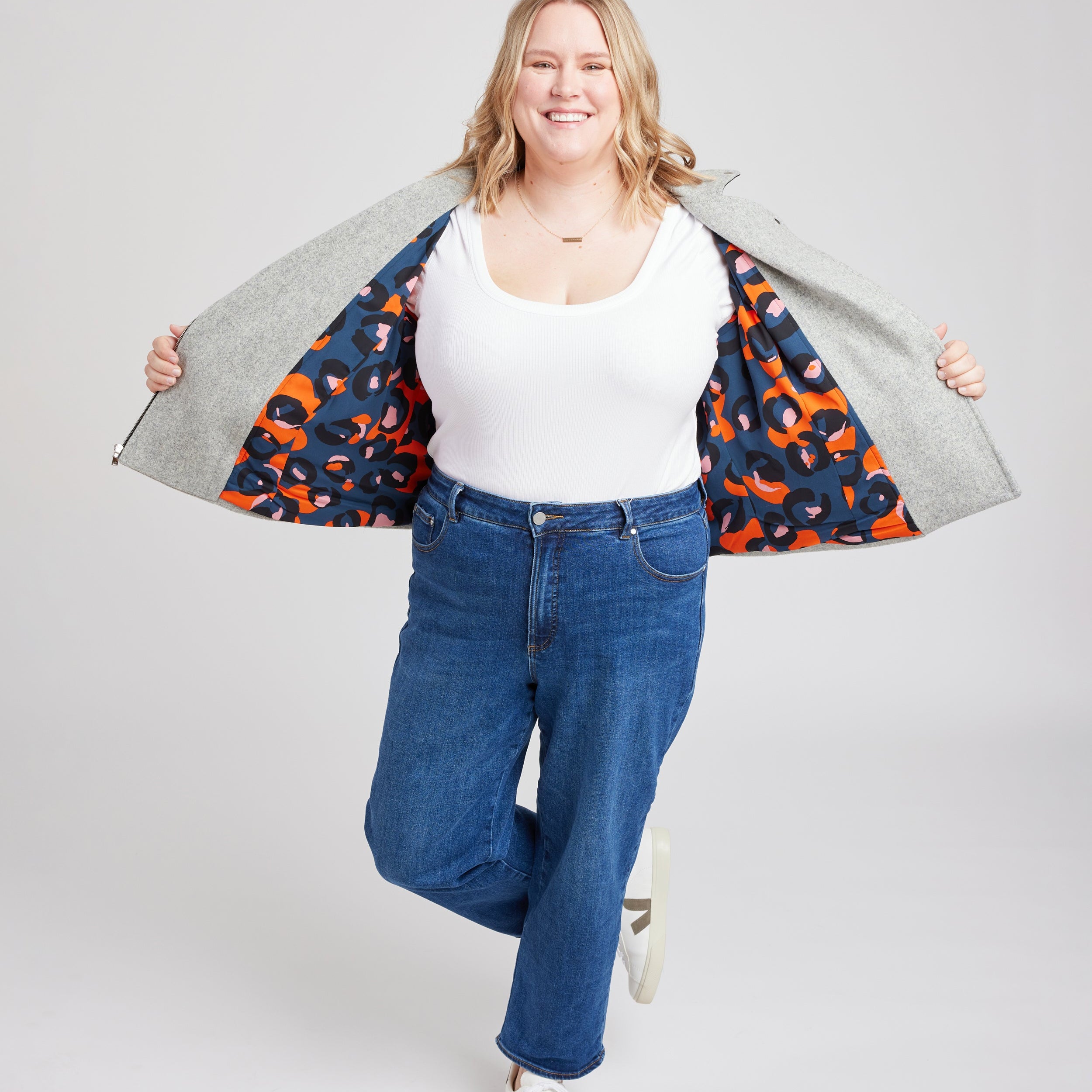 Woman wearing a white top, blue jeans, and a colorful jacket over her shoulders on a plain background. This biker jacket is the Canton Moto Jacket sewing pattern from Cashmerette.