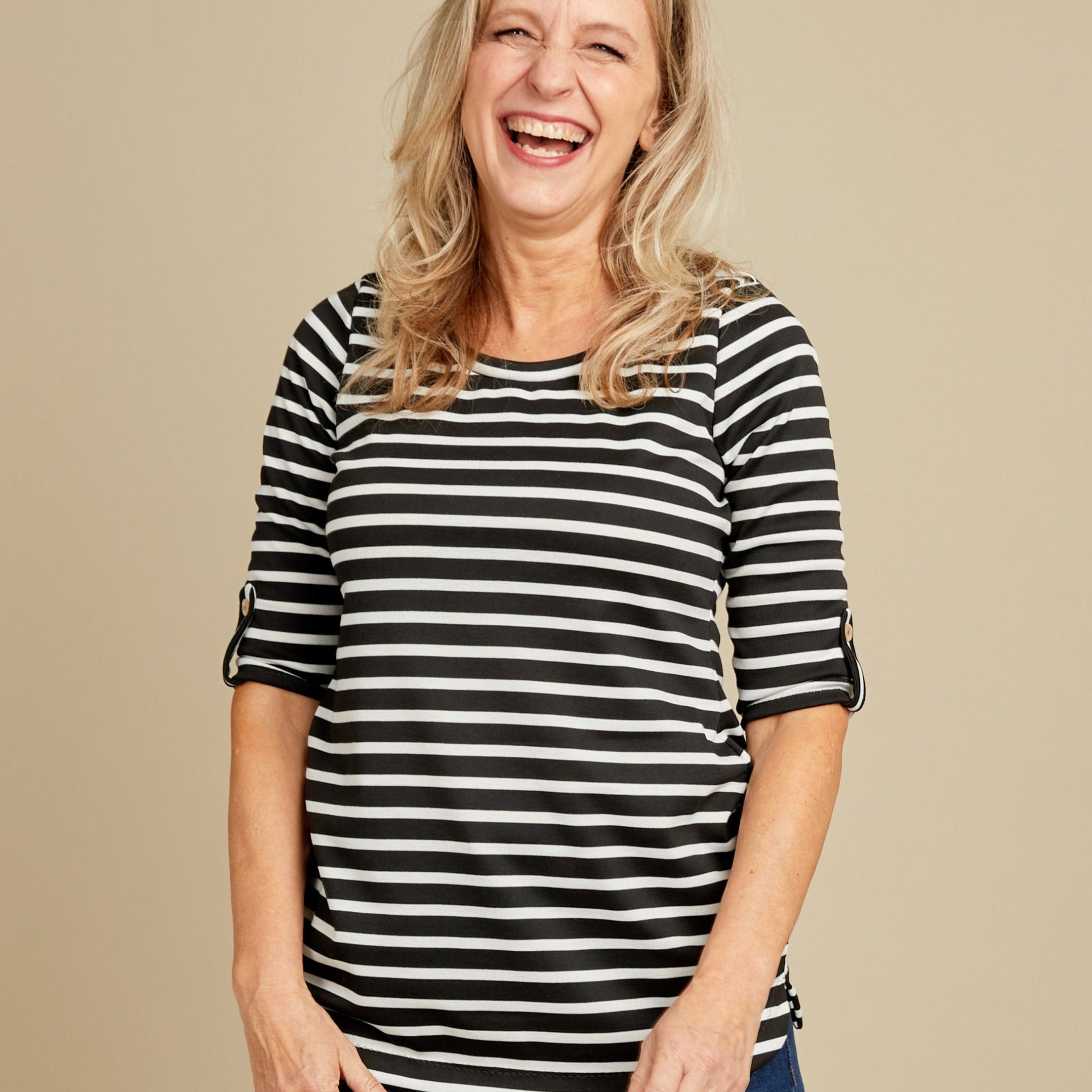 Woman wearing a black and white striped shirt and blue jeans on a beige background. This t-shirt is the Concord T-Shirt sewing pattern from Cashmerette.