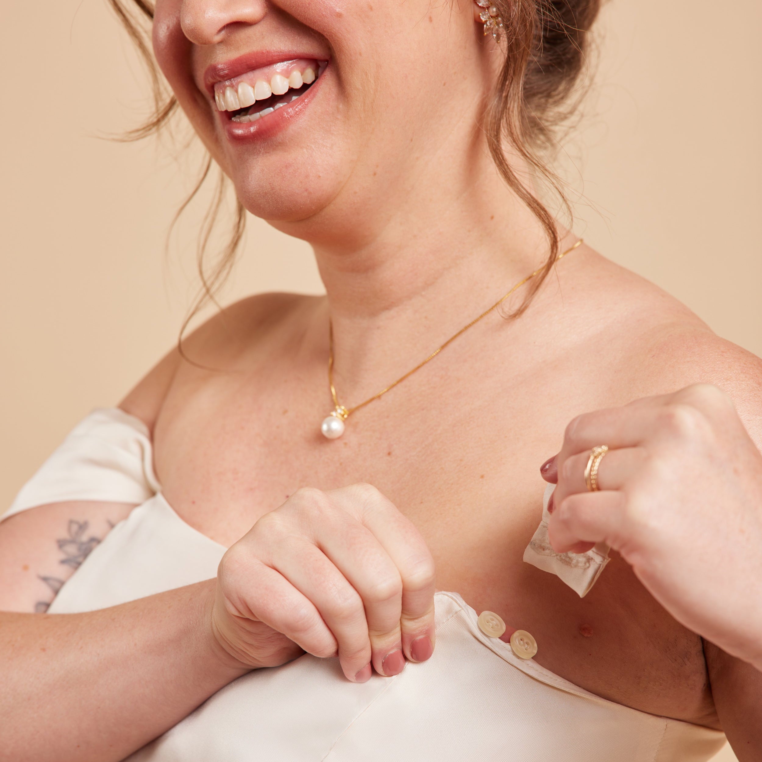 Woman wearing a gold necklace with a pearl pendant against a beige background. This dress is the Ellington Strapless Dress sewing pattern from Cashmerette.