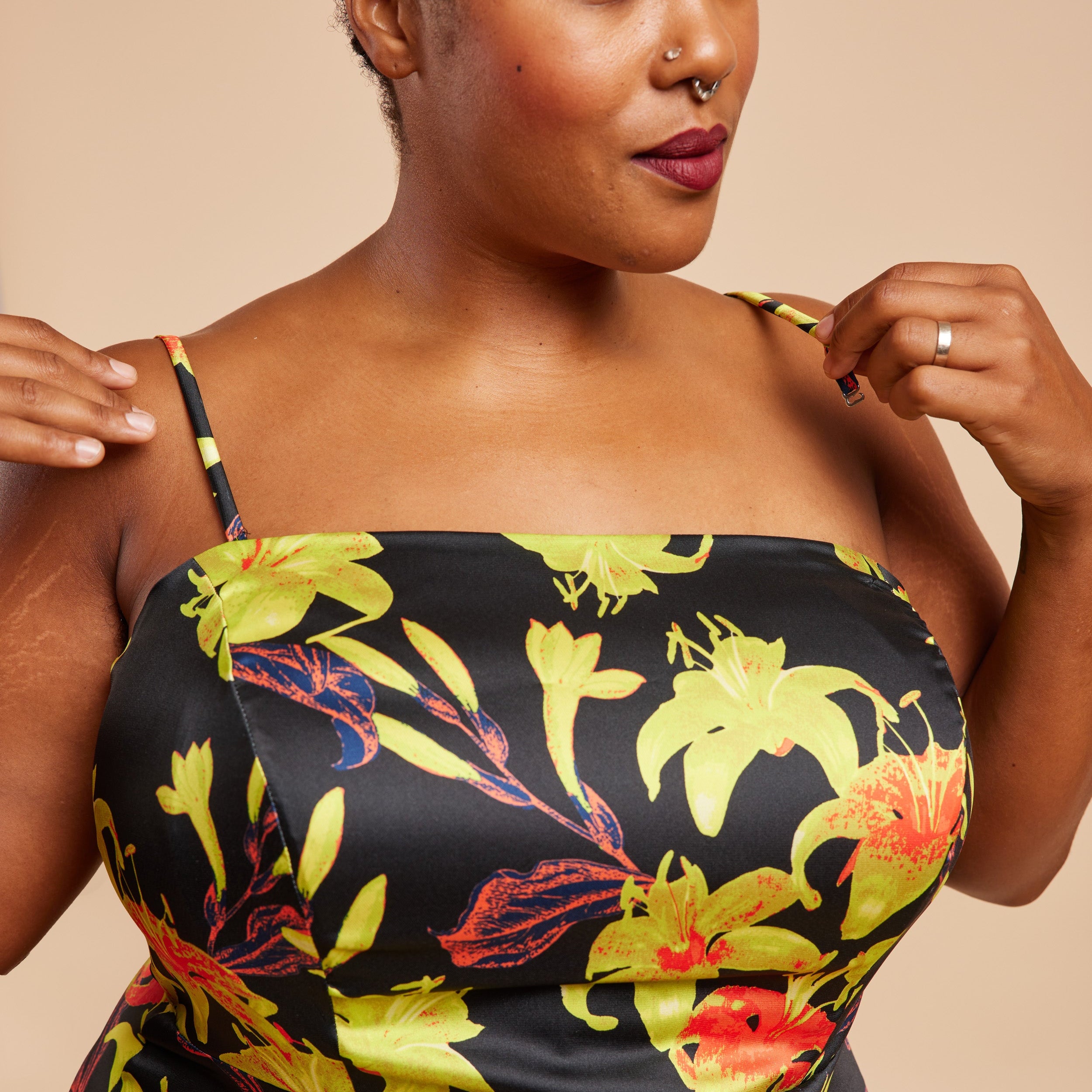 Woman wearing a black dress with colorful floral patterns on a beige background. This dress is the Ellington Strapless Dress sewing pattern from Cashmerette.
