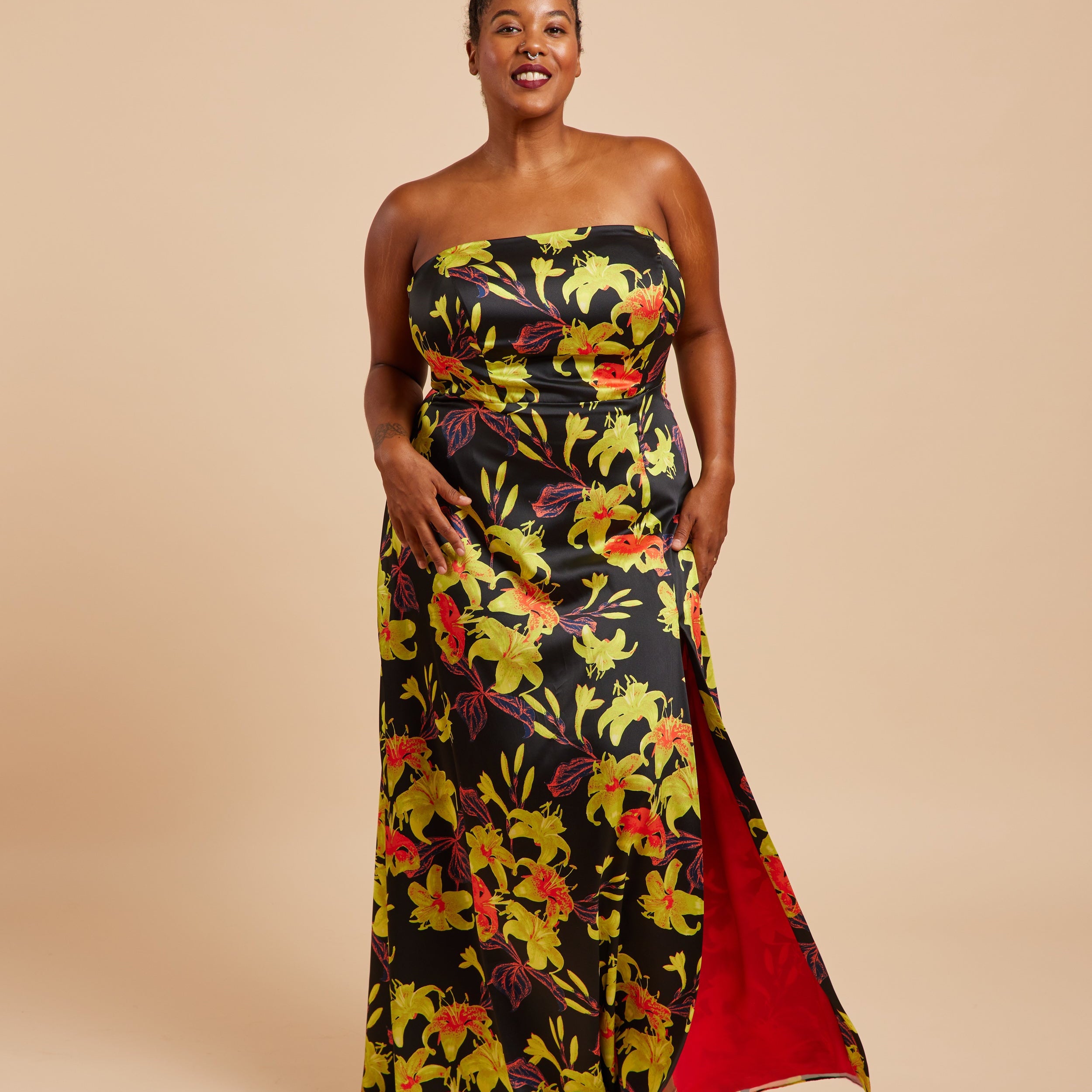 Woman wearing a strapless floral dress with a red lining on a beige background. This dress is the Ellington Strapless Dress sewing pattern from Cashmerette.