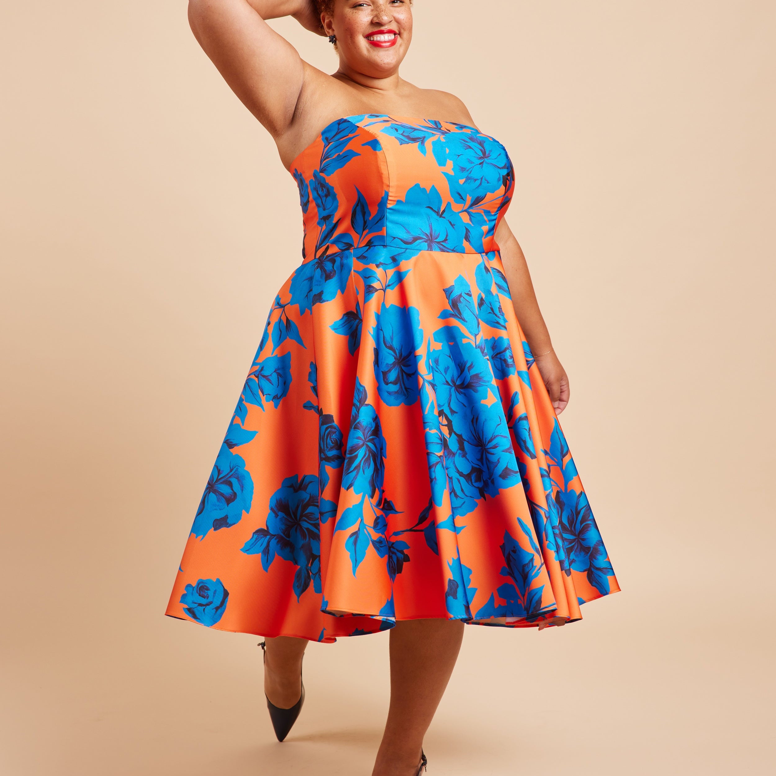 Woman wearing a strapless dress with orange and blue floral pattern on a beige background. This dress is the Ellington Strapless Dress sewing pattern from Cashmerette.