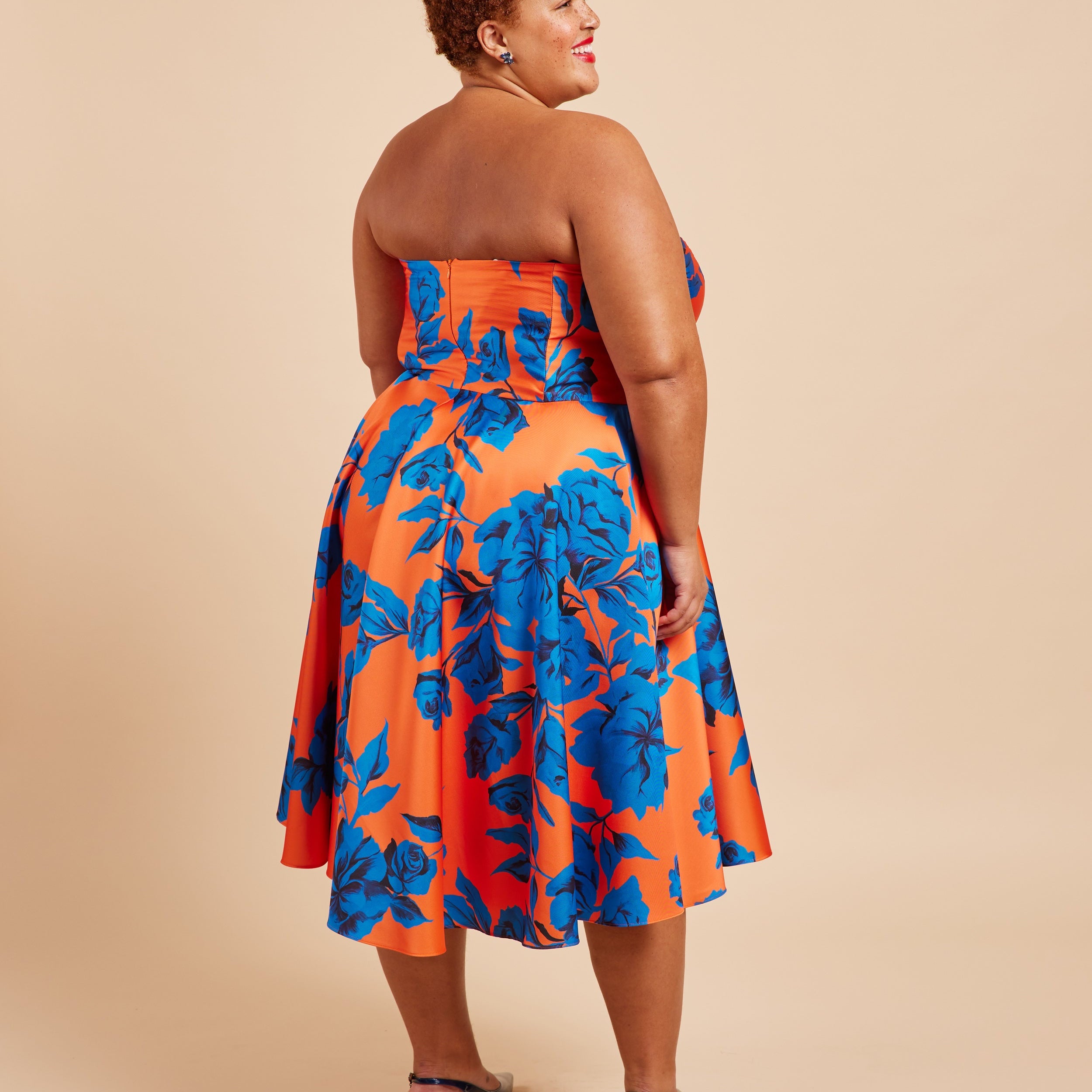 Woman wearing a strapless dress with blue and orange floral pattern on a beige background. This dress is the Ellington Strapless Dress sewing pattern from Cashmerette.