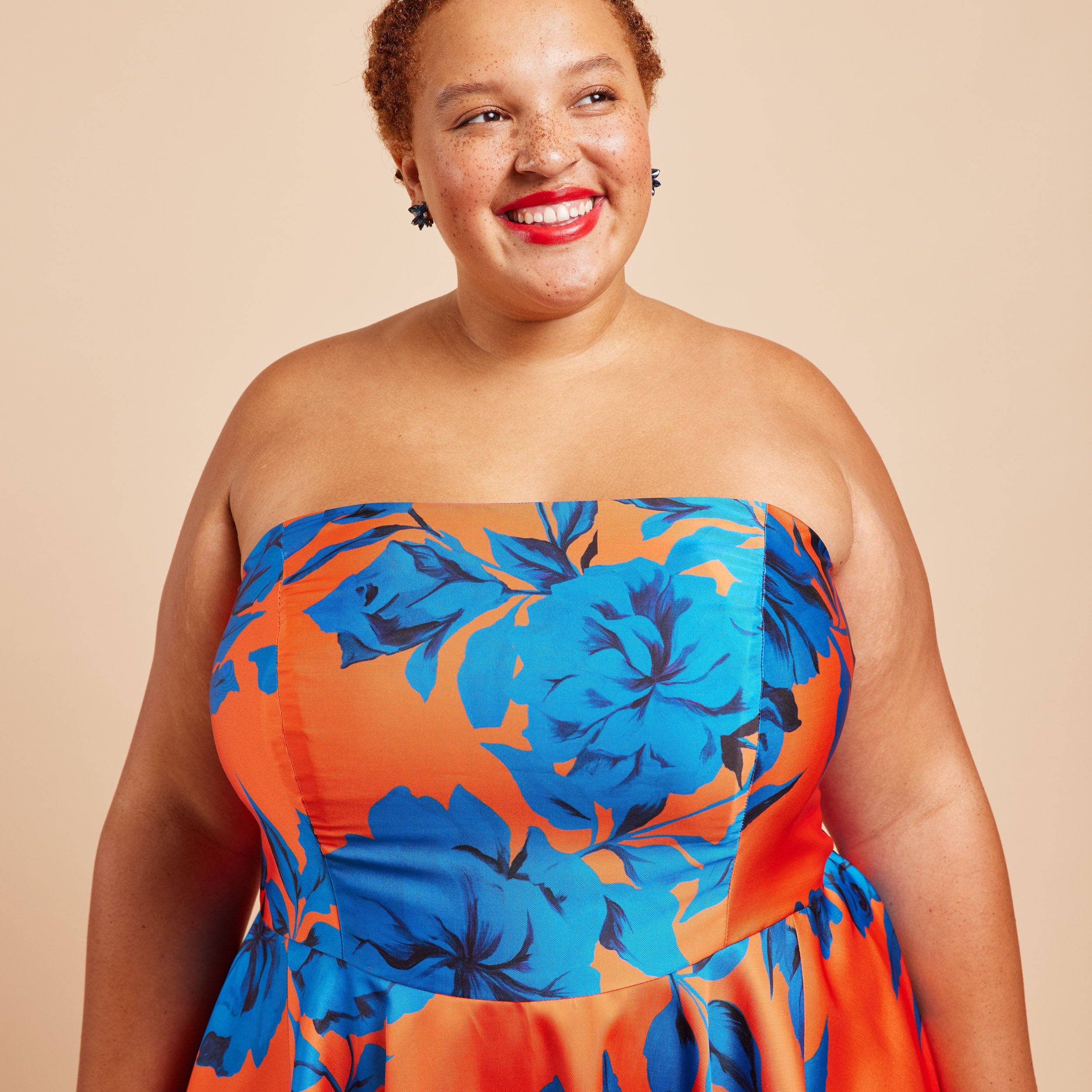 Woman wearing a strapless dress with blue floral pattern on a beige background. This dress is the Ellington Strapless Dress sewing pattern from Cashmerette.