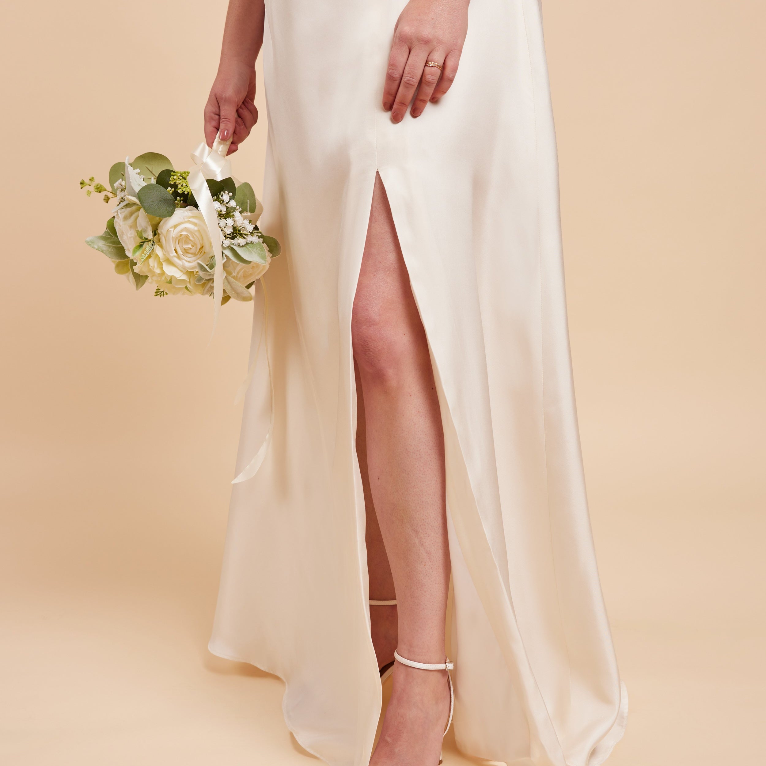 Woman in a white wedding dress with a high slit holding a bouquet on a beige background. This dress is the Ellington Strapless Dress sewing pattern from Cashmerette.