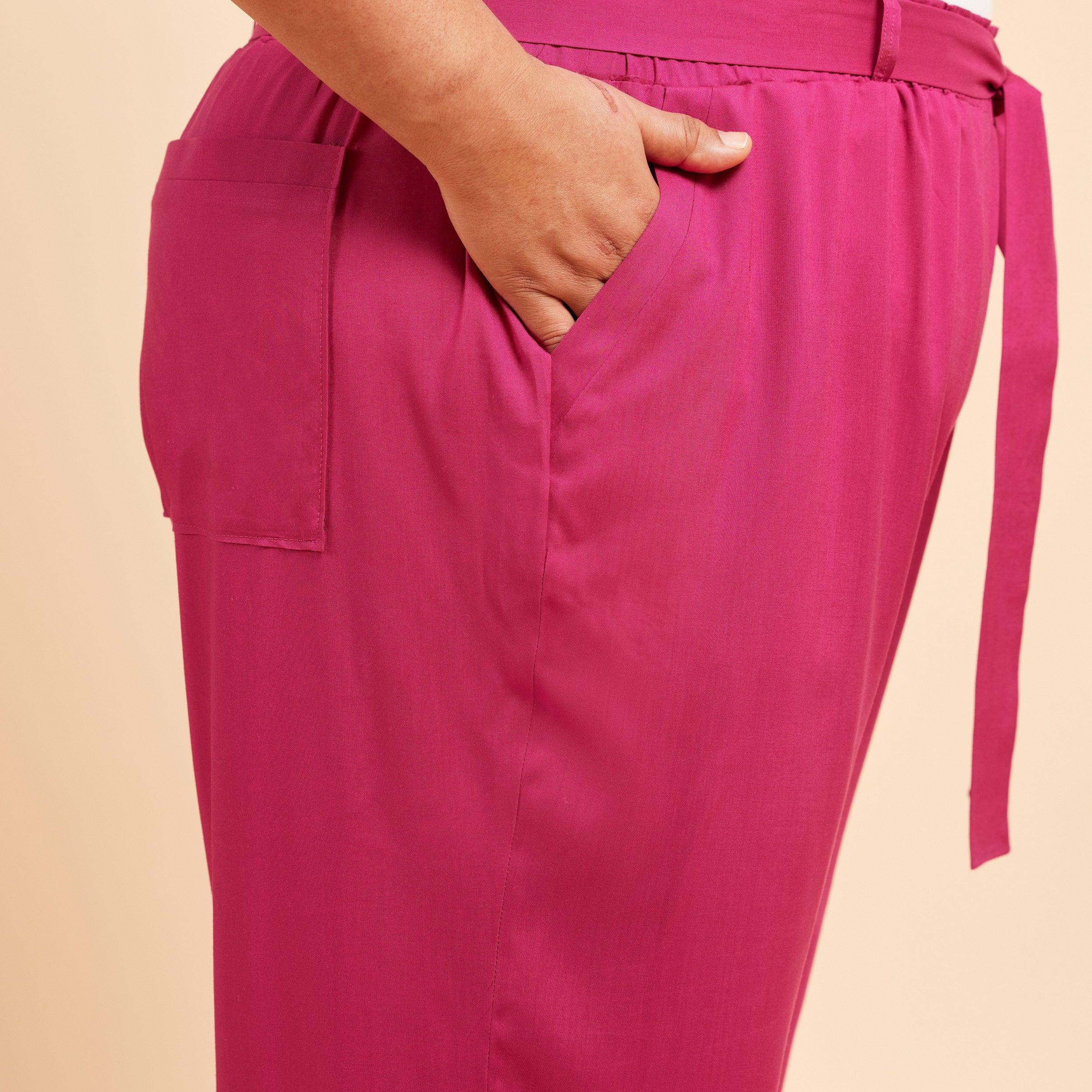 Pink pants with a belt on a beige background. These pants are the Everett Pants & Shorts sewing pattern from Cashmerette.