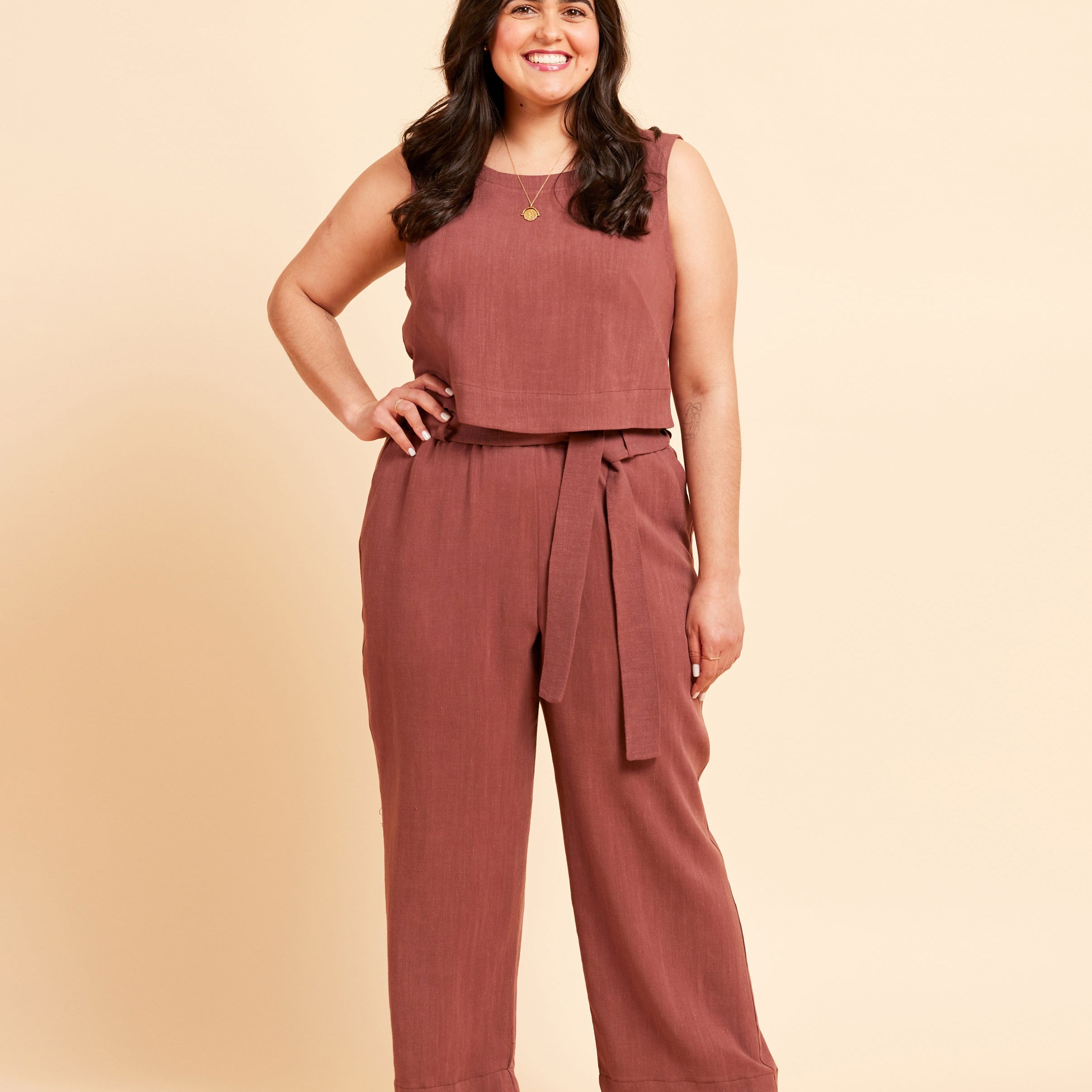Woman wearing a brown top and brown pants in front of a yellow background. These shorts are the Everett Pants & Shorts sewing pattern from Cashmerette.