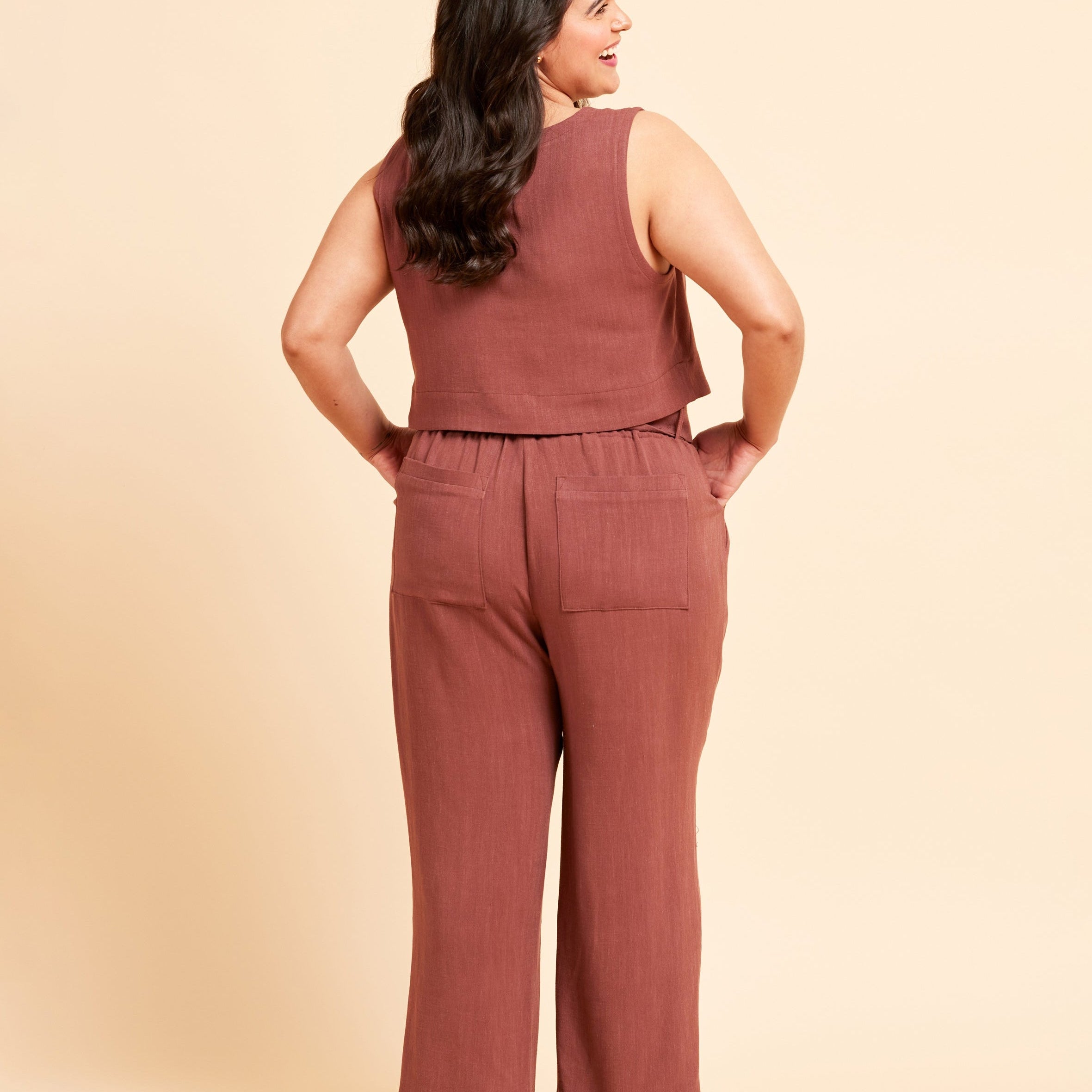 Woman wearing a brown sleeveless top and pants against a beige background. These pants are the Everett Pants & Shorts sewing pattern from Cashmerette.