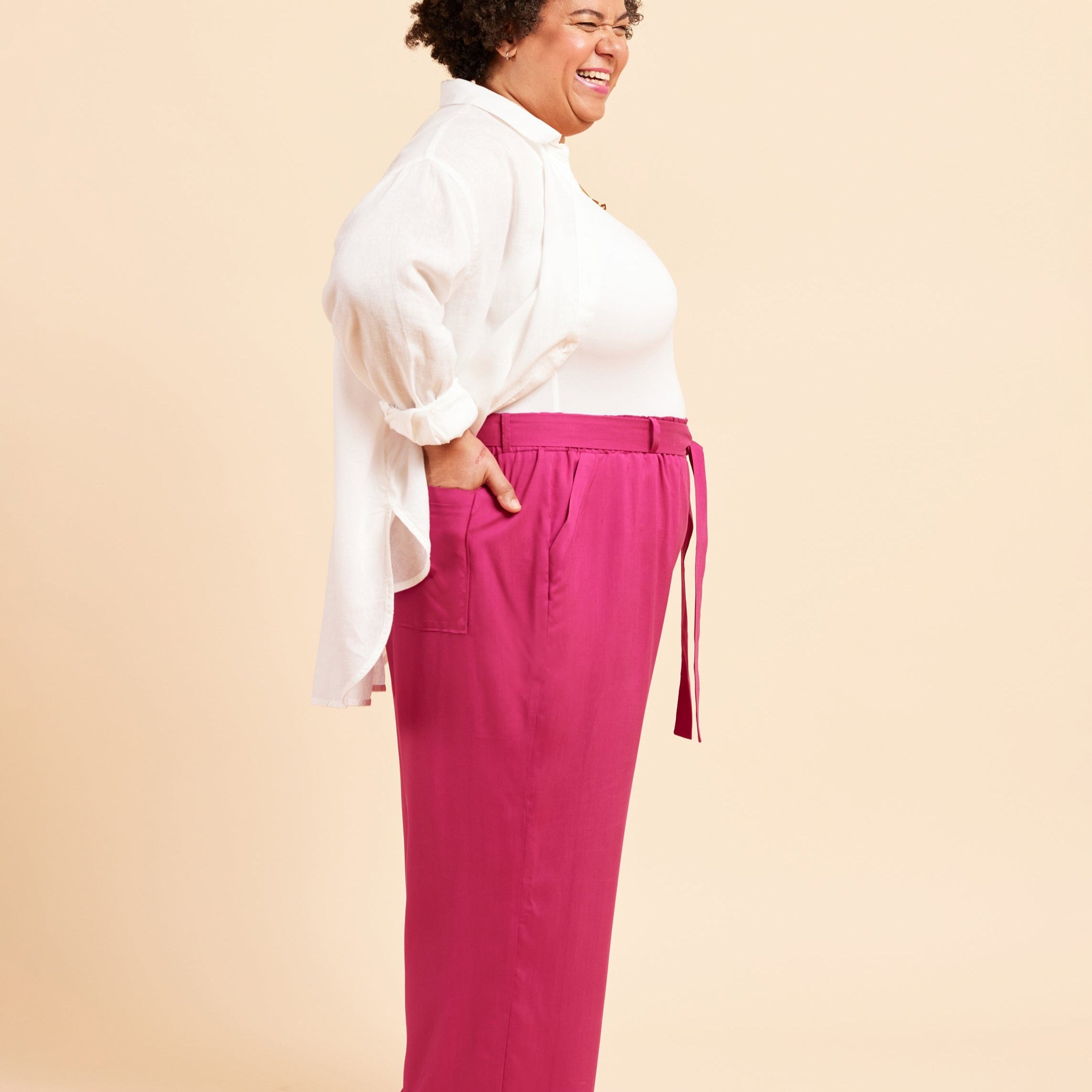 Woman wearing a white blouse and pink pants on a beige background. These pants are the Everett Pants & Shorts sewing pattern from Cashmerette.