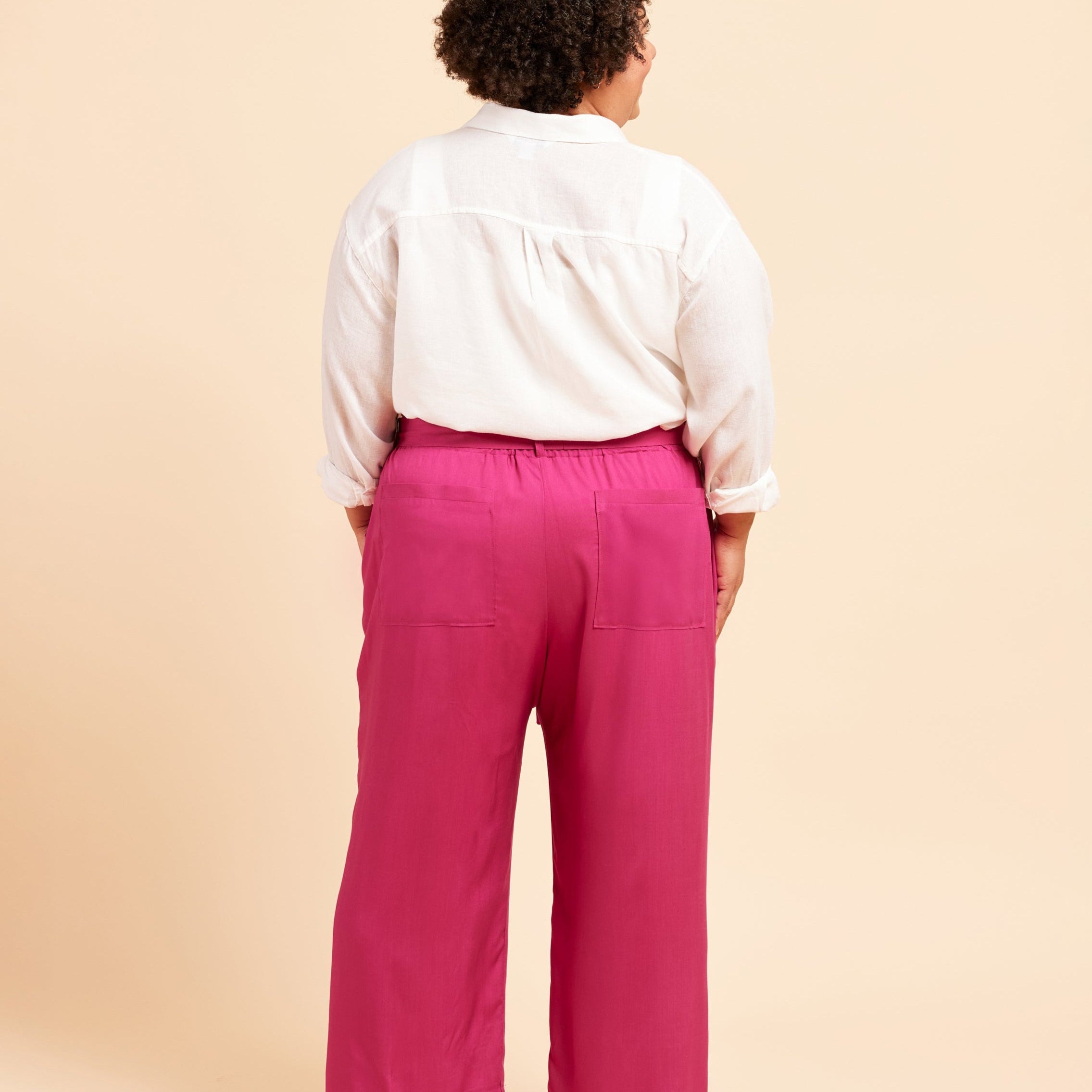 Person wearing a white shirt and pink pants on a beige background. These pants are the Everett Pants & Shorts sewing pattern from Cashmerette.