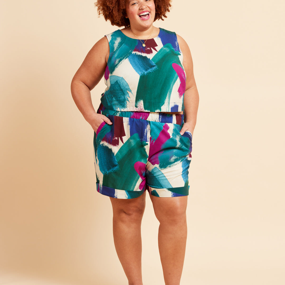 Woman wearing a colorful sleeveless top and shorts set on a beige background. These shorts are the Everett Pants & Shorts sewing pattern from Cashmerette.