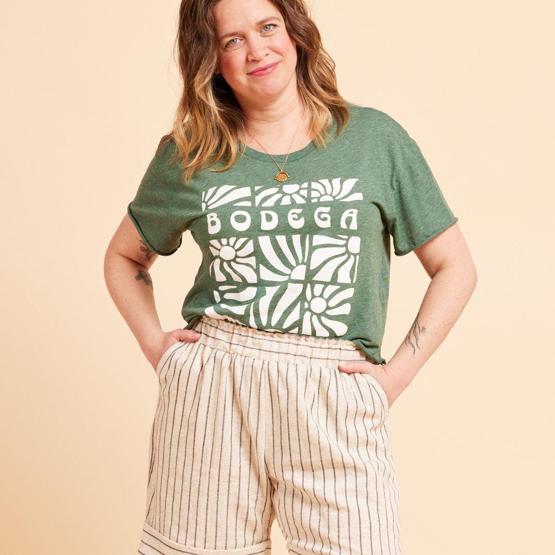 Woman wearing a green t-shirt with 'BODEGA' print and beige shorts on a beige background. These shorts are the Everett Pants & Shorts sewing pattern from Cashmerette.