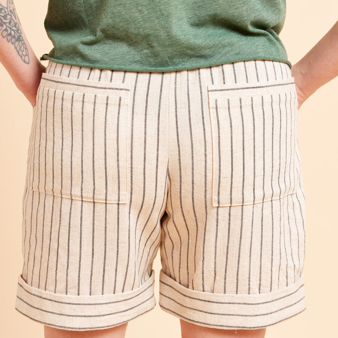 Beige shorts with black stripes worn by a person on a beige background. These shorts are the Everett Pants & Shorts sewing pattern from Cashmerette.