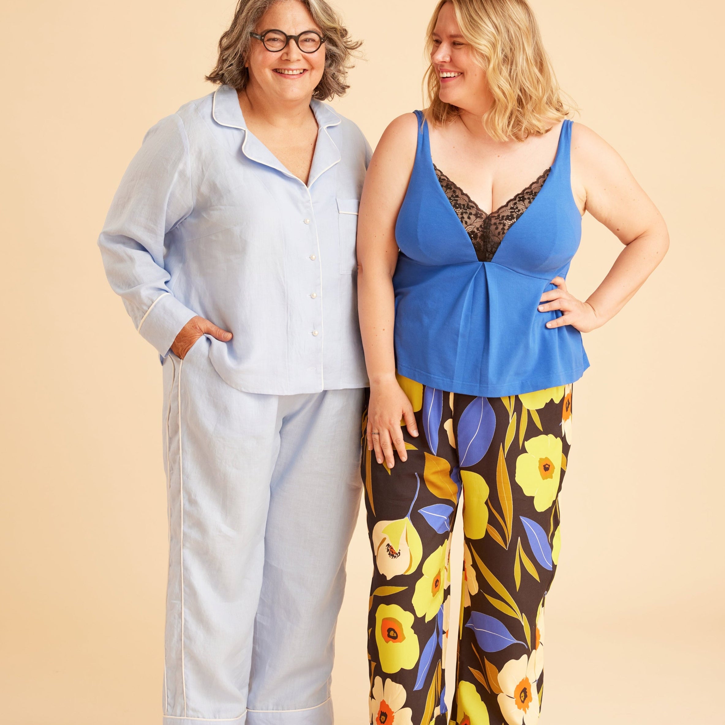 Two women standing side by side against a beige background, one in light blue outfit and the other in colorful floral pants. This is the Fiske Sleepwear Set sewing pattern from Cashmerette.