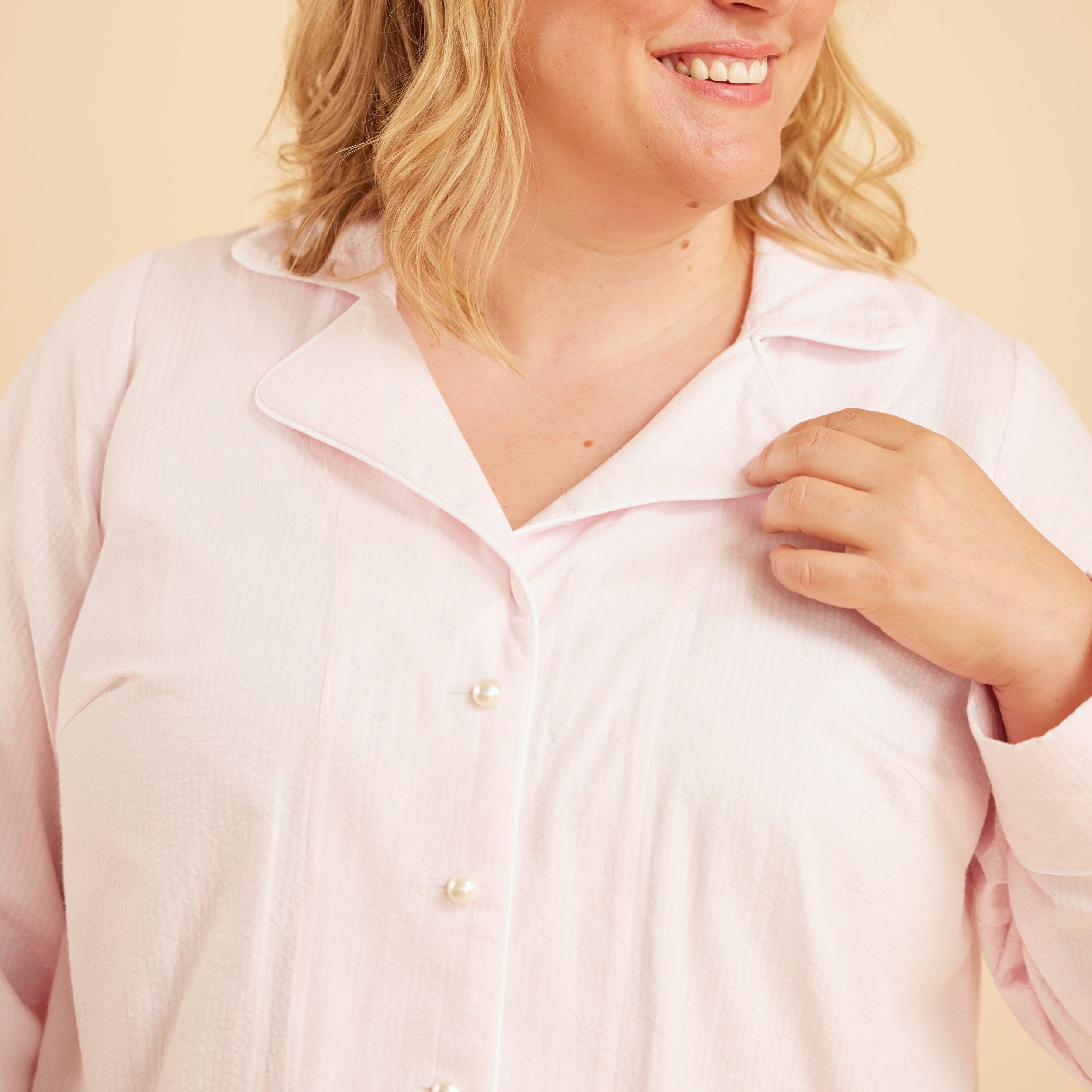 Woman wearing a light pink shirt against a beige background. This is the Fiske Sleepwear Set sewing pattern from Cashmerette.