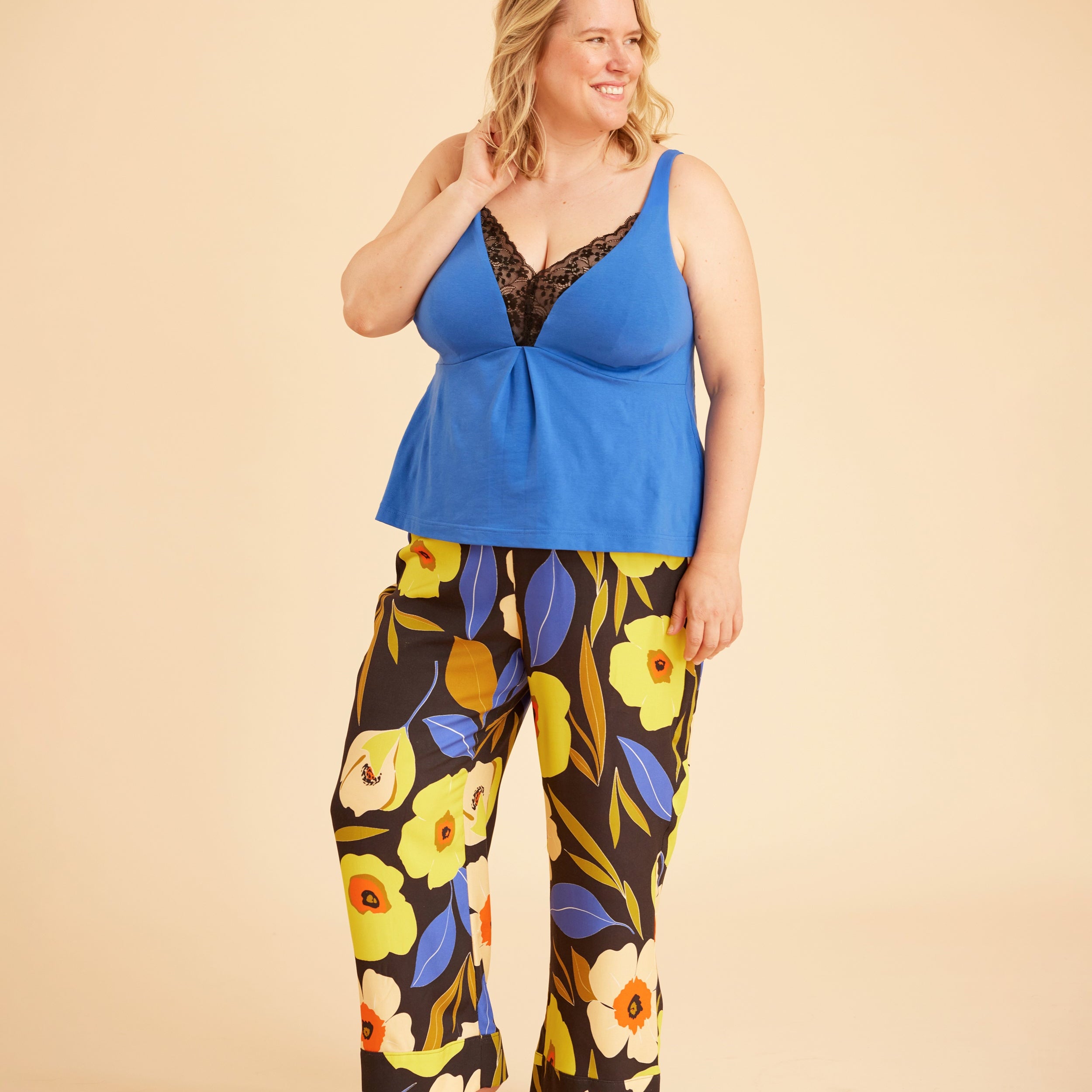 Woman wearing a blue top and floral pants on a beige background. This is the Fiske Sleepwear Set sewing pattern from Cashmerette.