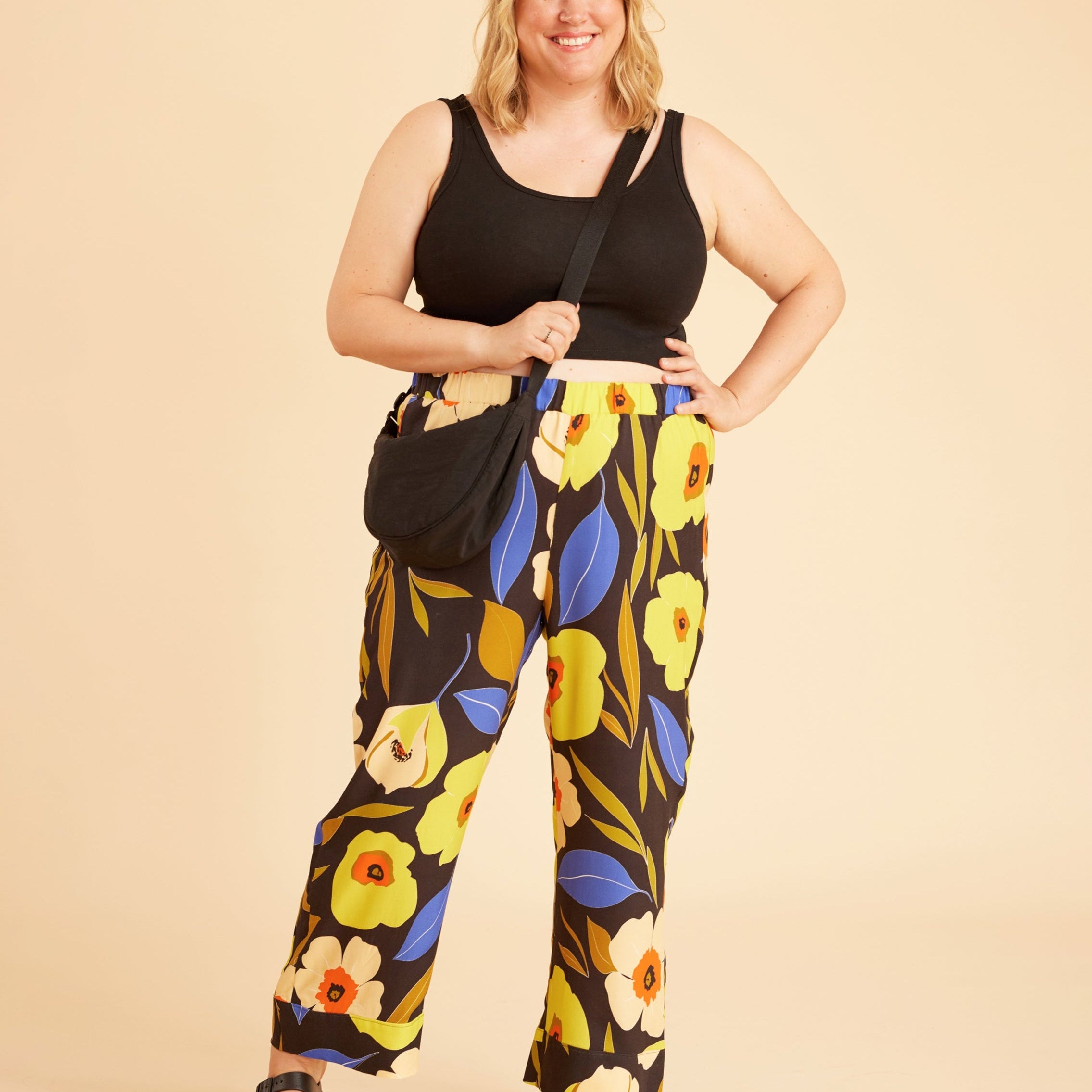 Woman wearing a black tank top and floral pants against a beige background. This is the Fiske Sleepwear Set sewing pattern from Cashmerette.