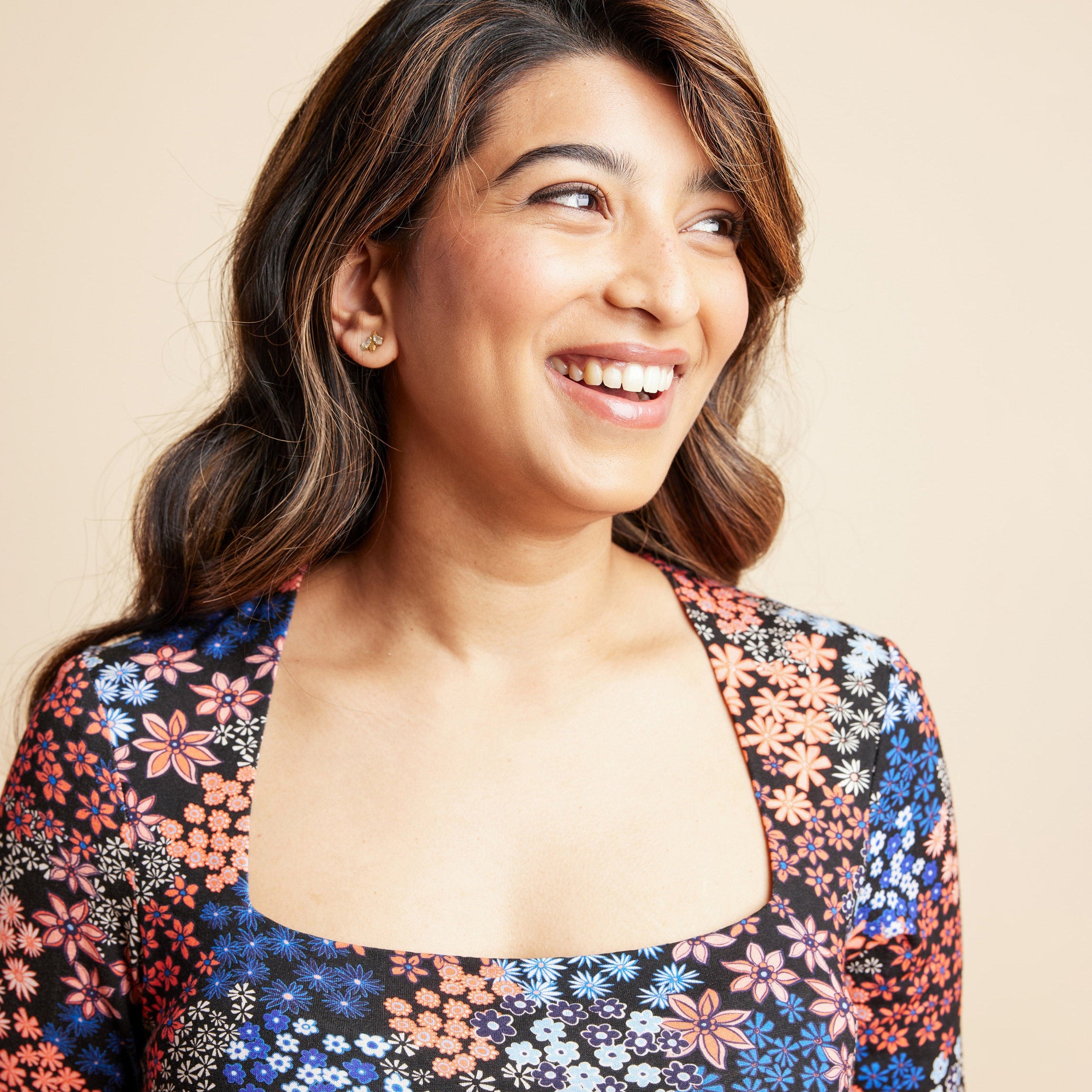 Woman wearing a floral top against a beige background. This is the Grafton Dress, Top & Skirt sewing pattern from Cashmrette.