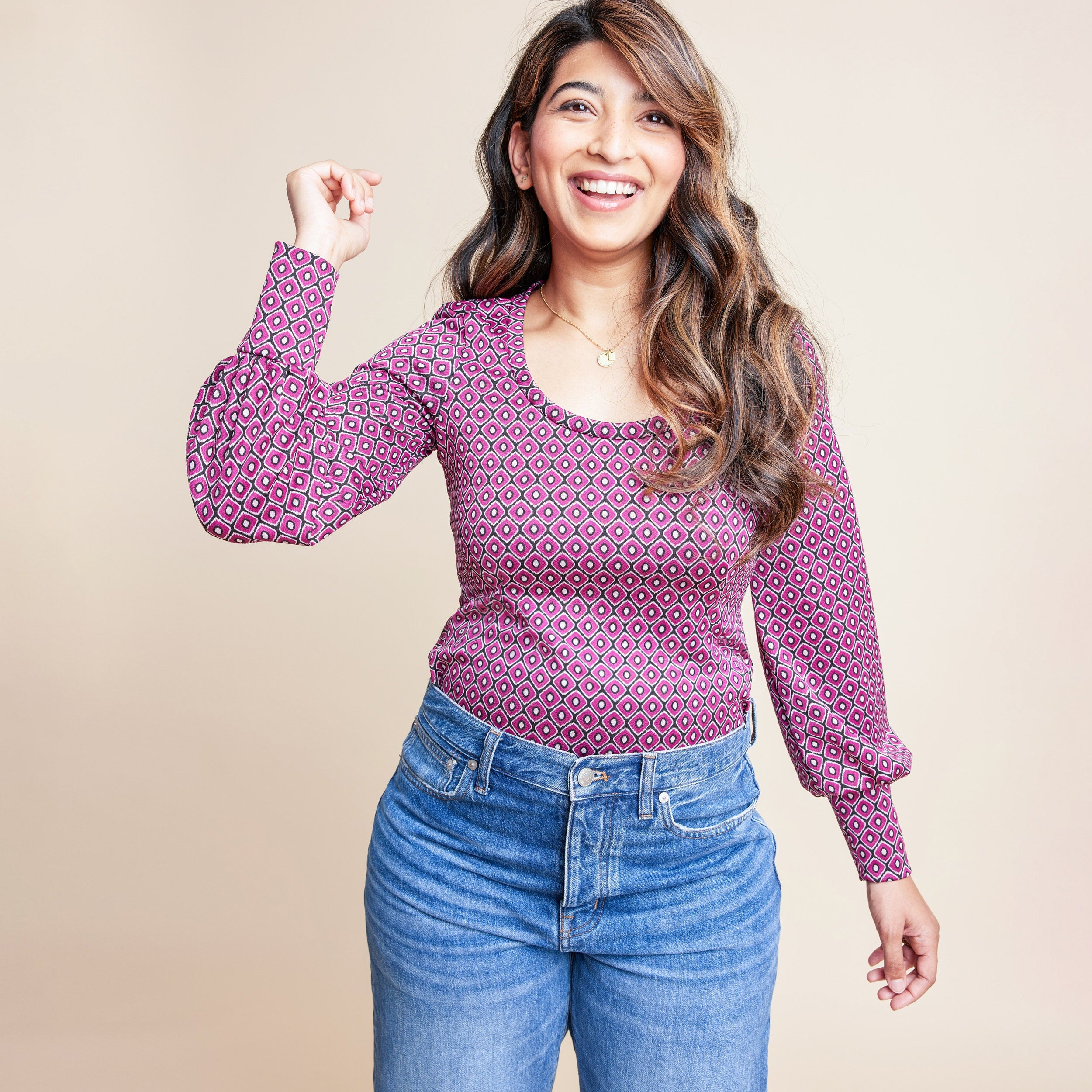 Woman wearing a patterned pink long-sleeve top and blue jeans against a beige background. This is the Grafton Dress, Top & Skirt sewing pattern from Cashmrette.