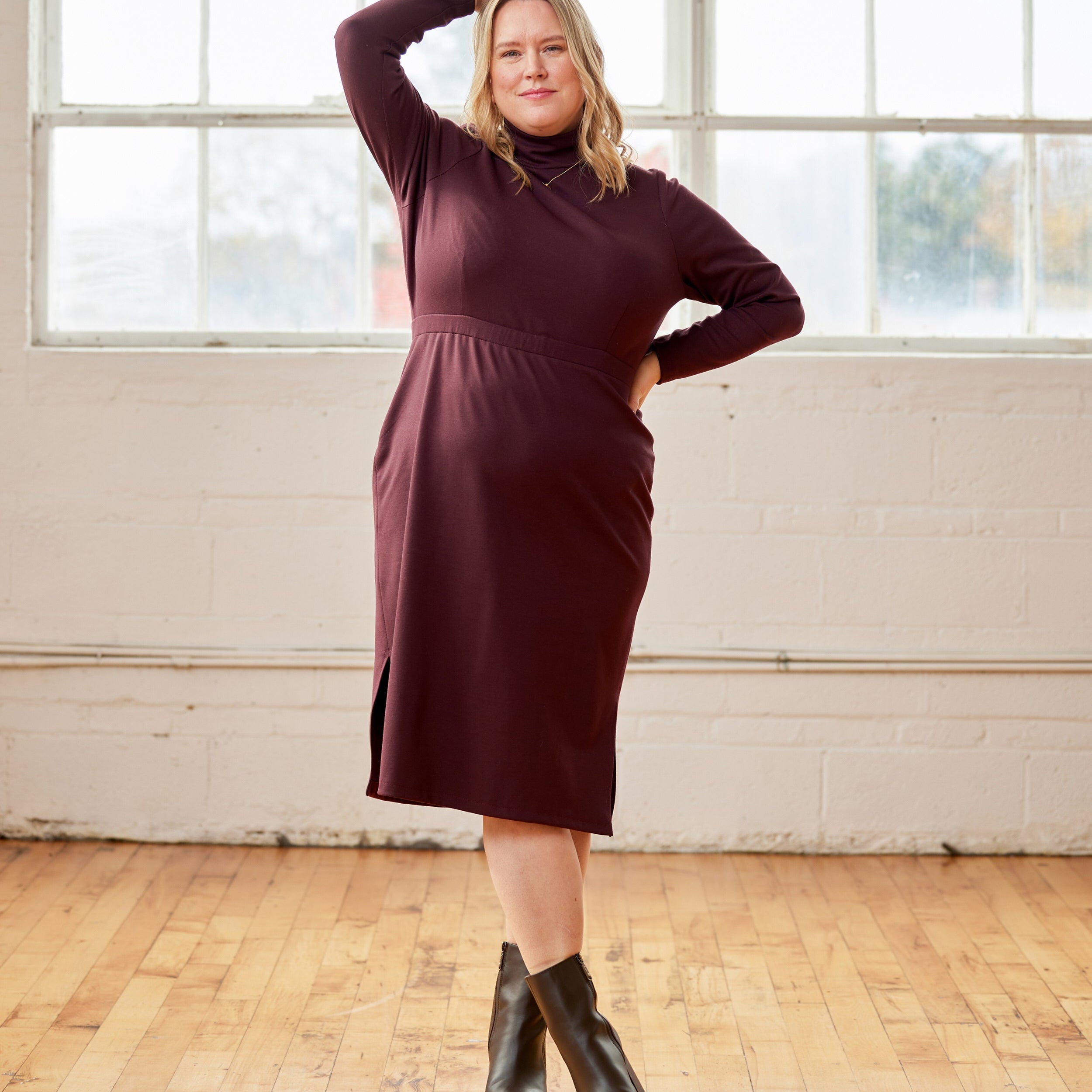 Woman wearing a burgundy dress standing in a room with large windows and wooden floor. This is the Grafton Dress, Top & Skirt sewing pattern from Cashmerette.