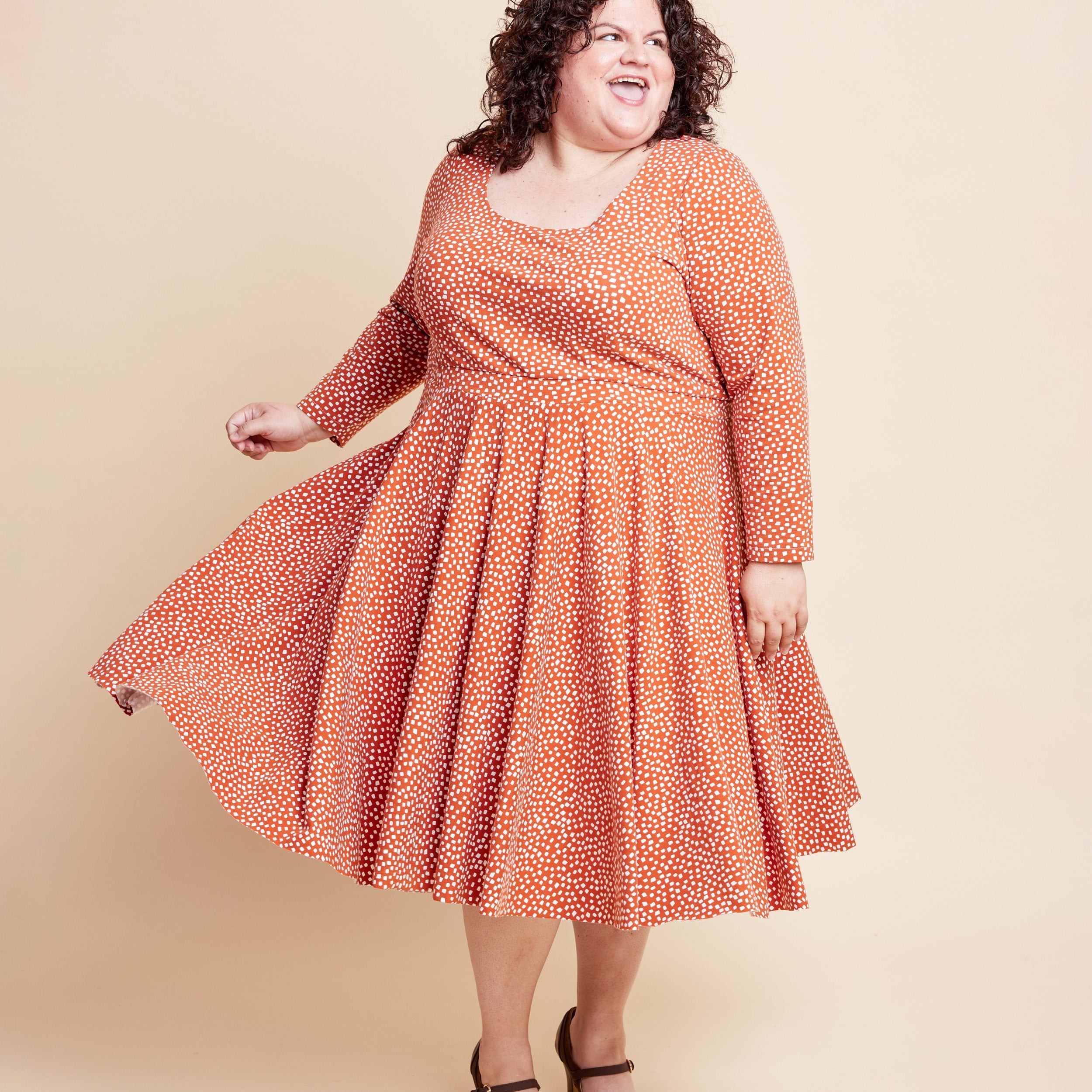 Woman wearing an orange patterned dress against a beige background. This is the Grafton Dress, Top & Skirt sewing pattern from Cashmerette.