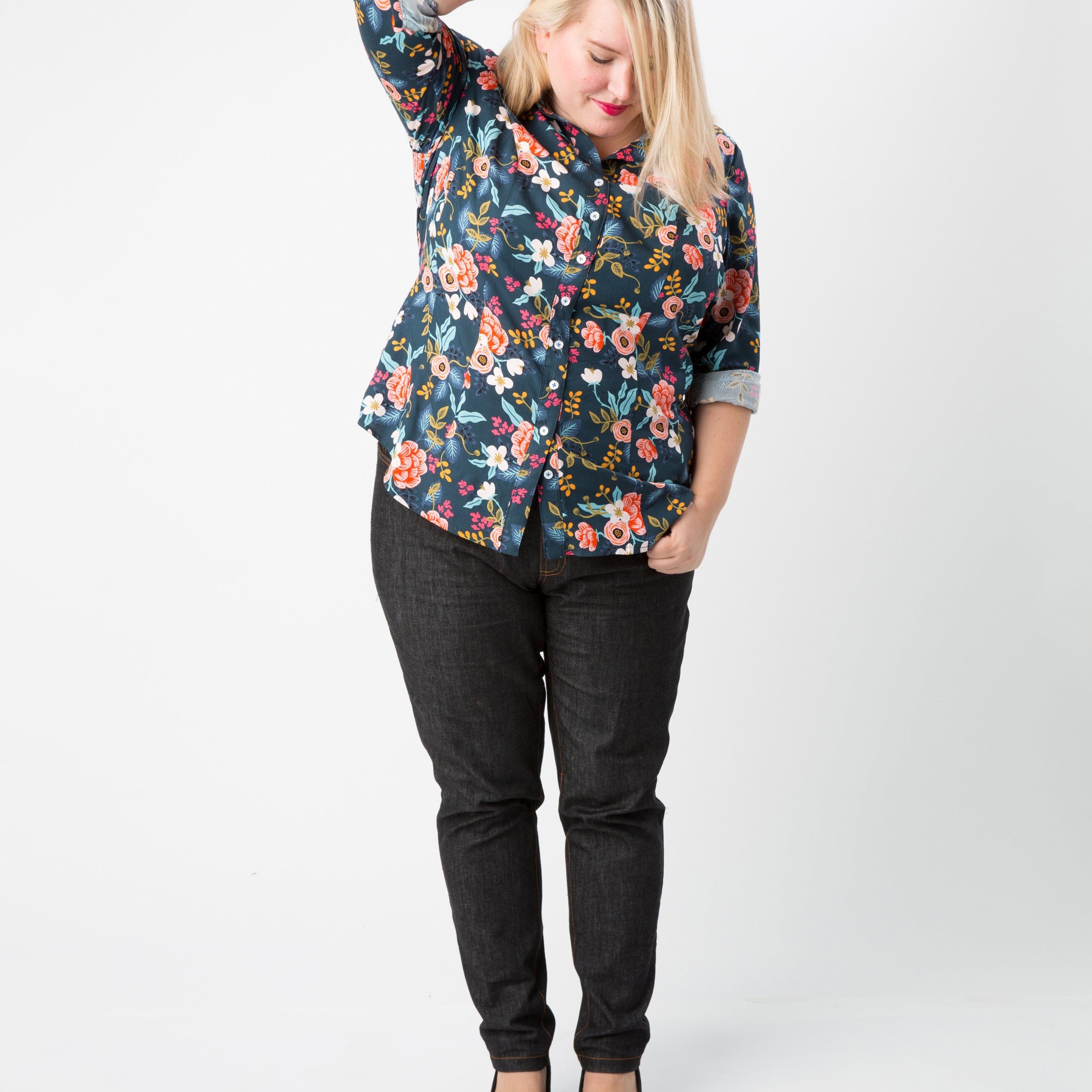 Woman wearing a floral blouse and black pants on a white background. This button-up shirt is the Harrison Shirt sewing pattern from Cashmerette.