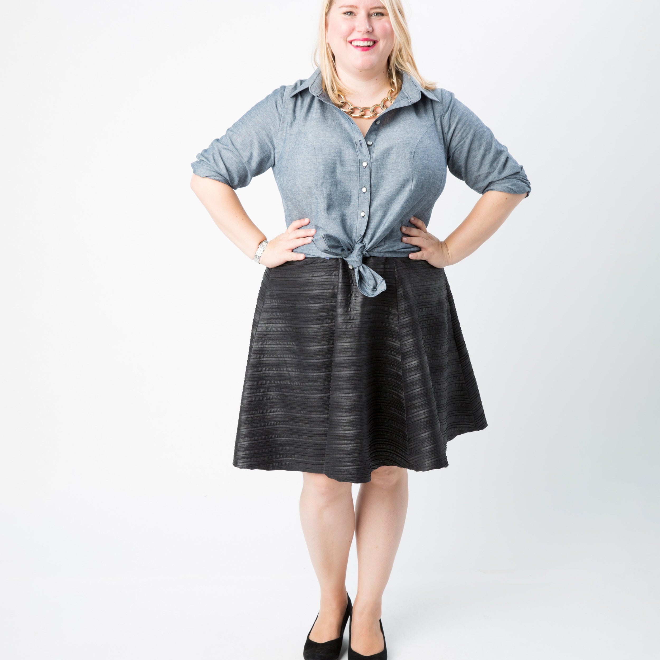 Woman wearing a blue shirt and black skirt on a white background. This button-up shirt is the Harrison Shirt sewing pattern from Cashmerette.