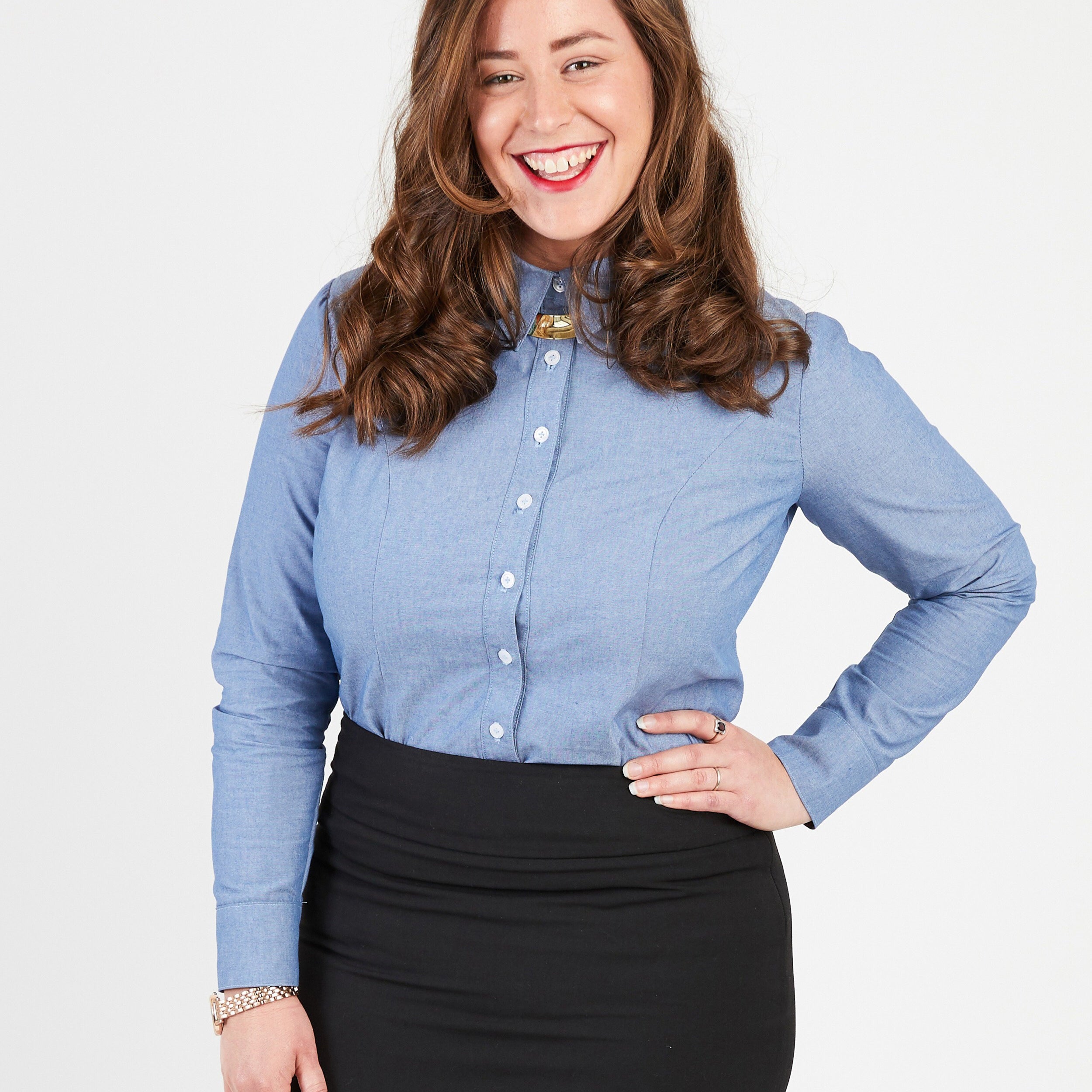 Woman wearing a blue button-up shirt and black skirt on a white background. This button-up shirt is the Harrison Shirt sewing pattern from Cashmerette.