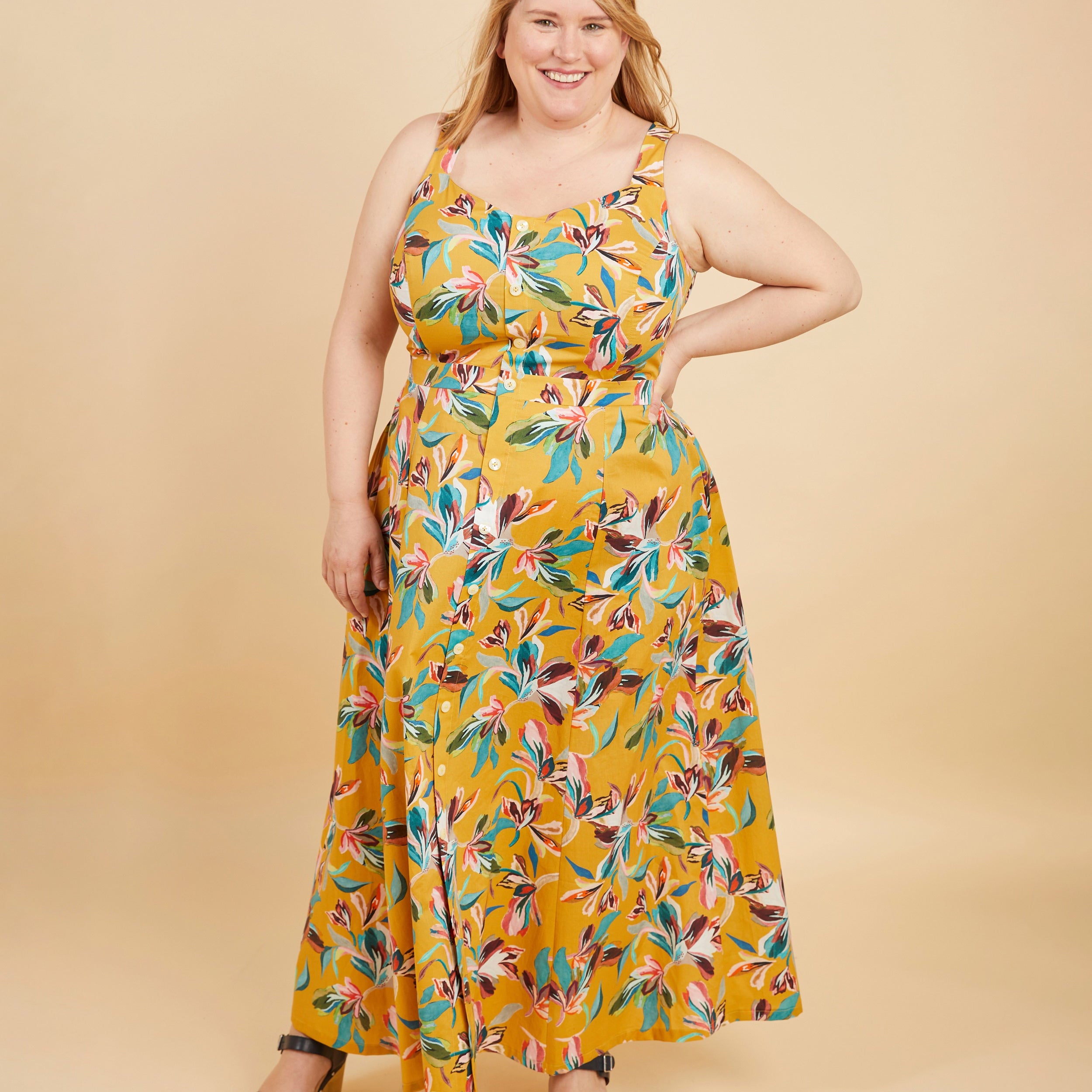 Woman wearing a yellow floral dress on a beige background. This is the Holyoke Maxi Dress & Skirt sewing pattern from Cashmerette.