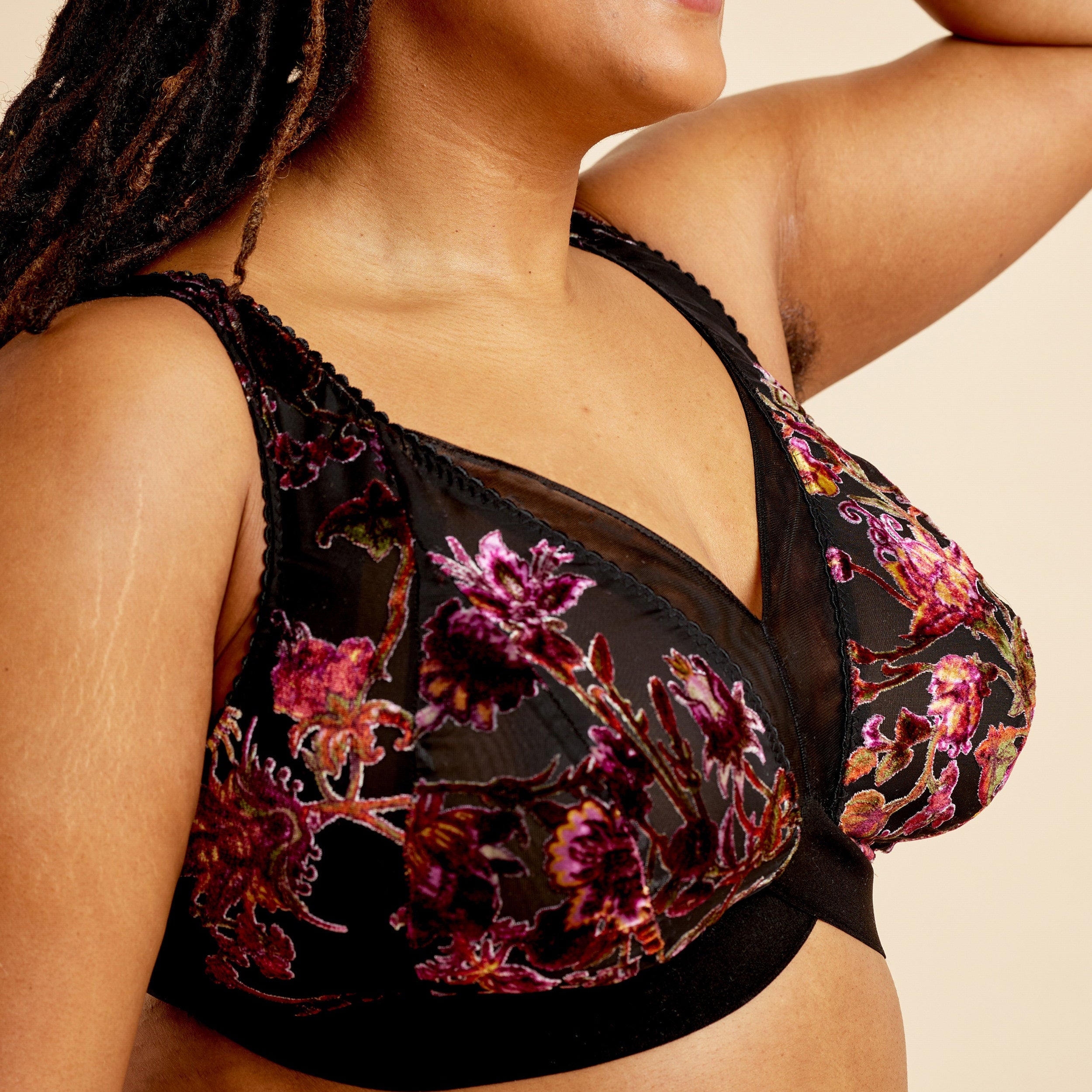Woman wearing a floral black bralette against a beige background. This bralette is the Loftus Bralette sewing pattern from Cashmerette.
