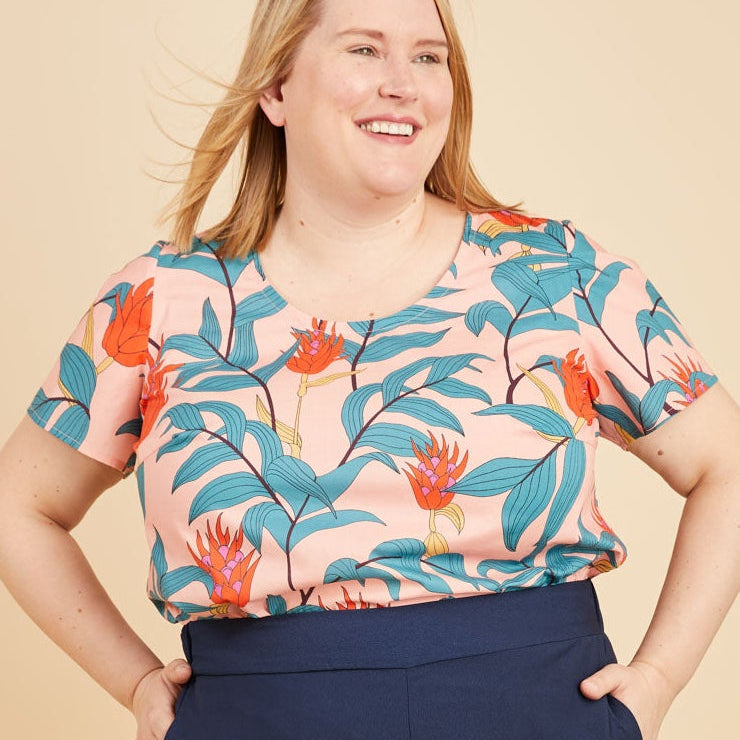 Woman wearing a colorful floral top and navy wide-leg pants on a beige background. This is the Montrose Top sewing pattern from Cashmerette.