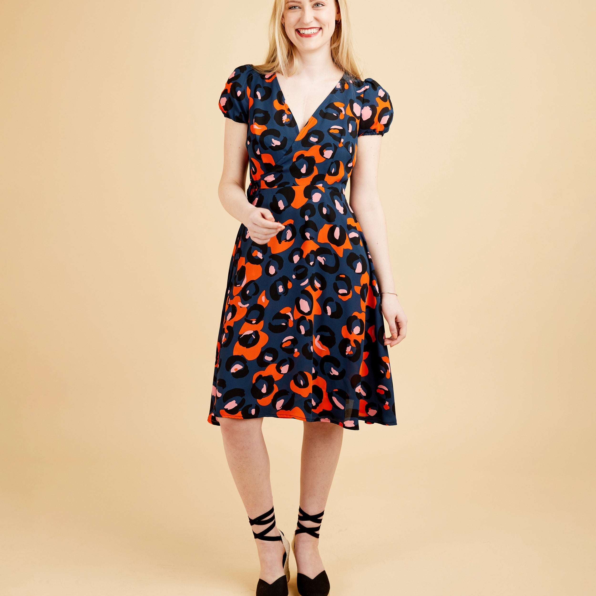 Woman wearing a patterned dress on a beige background. This dress is the Roseclair Wrap Dress sewing pattern from Cashmerette.