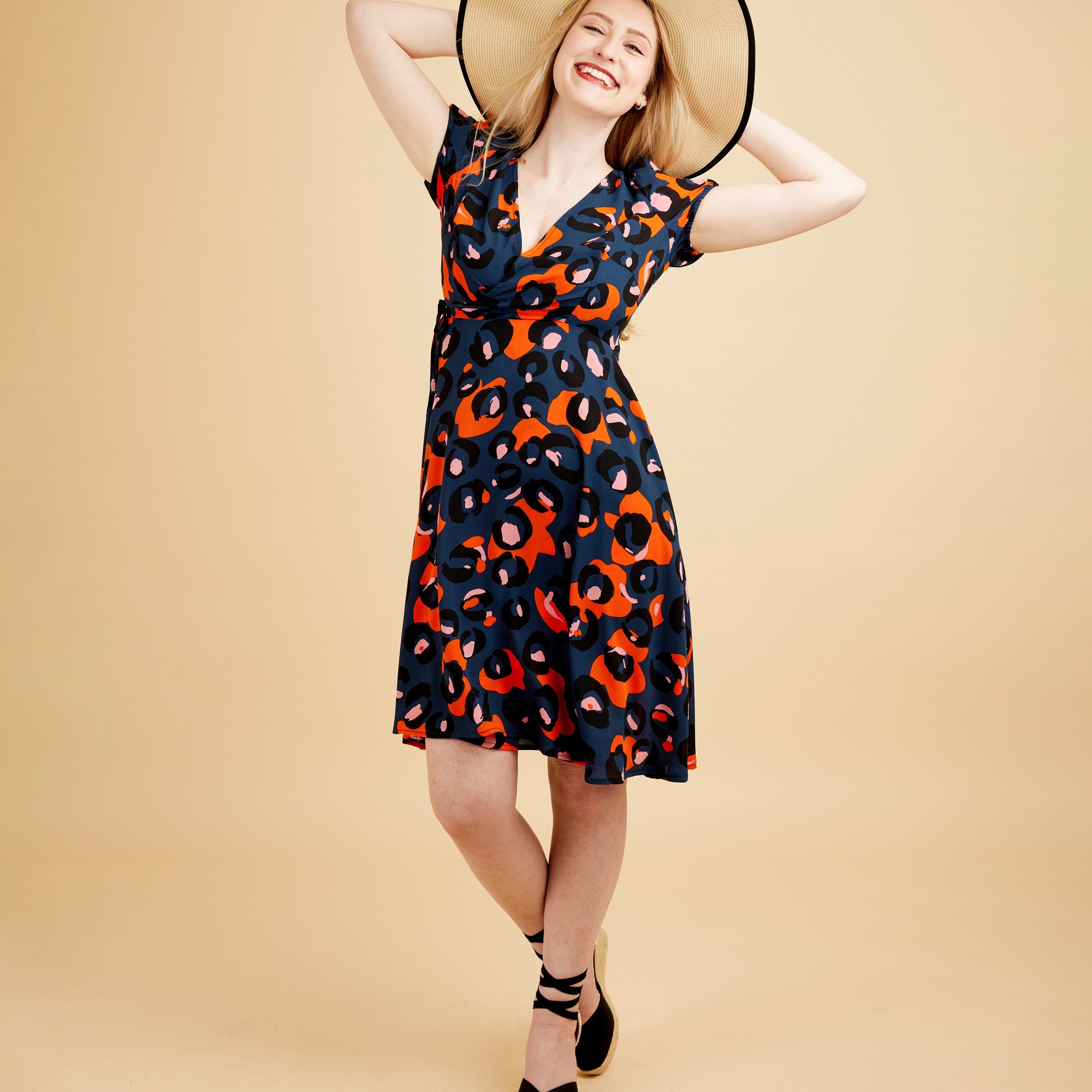 Woman wearing a patterned dress and wide-brimmed hat on a beige background. This dress is the Roseclair Wrap Dress sewing pattern from Cashmerette.