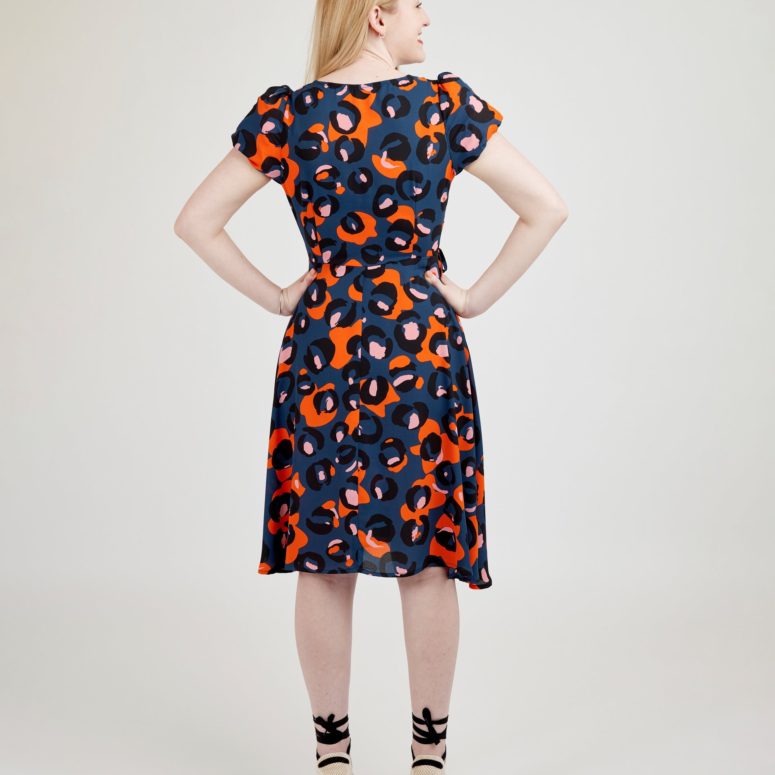 Woman wearing a patterned dress on a plain background. This dress is the Roseclair Wrap Dress sewing pattern from Cashmerette.