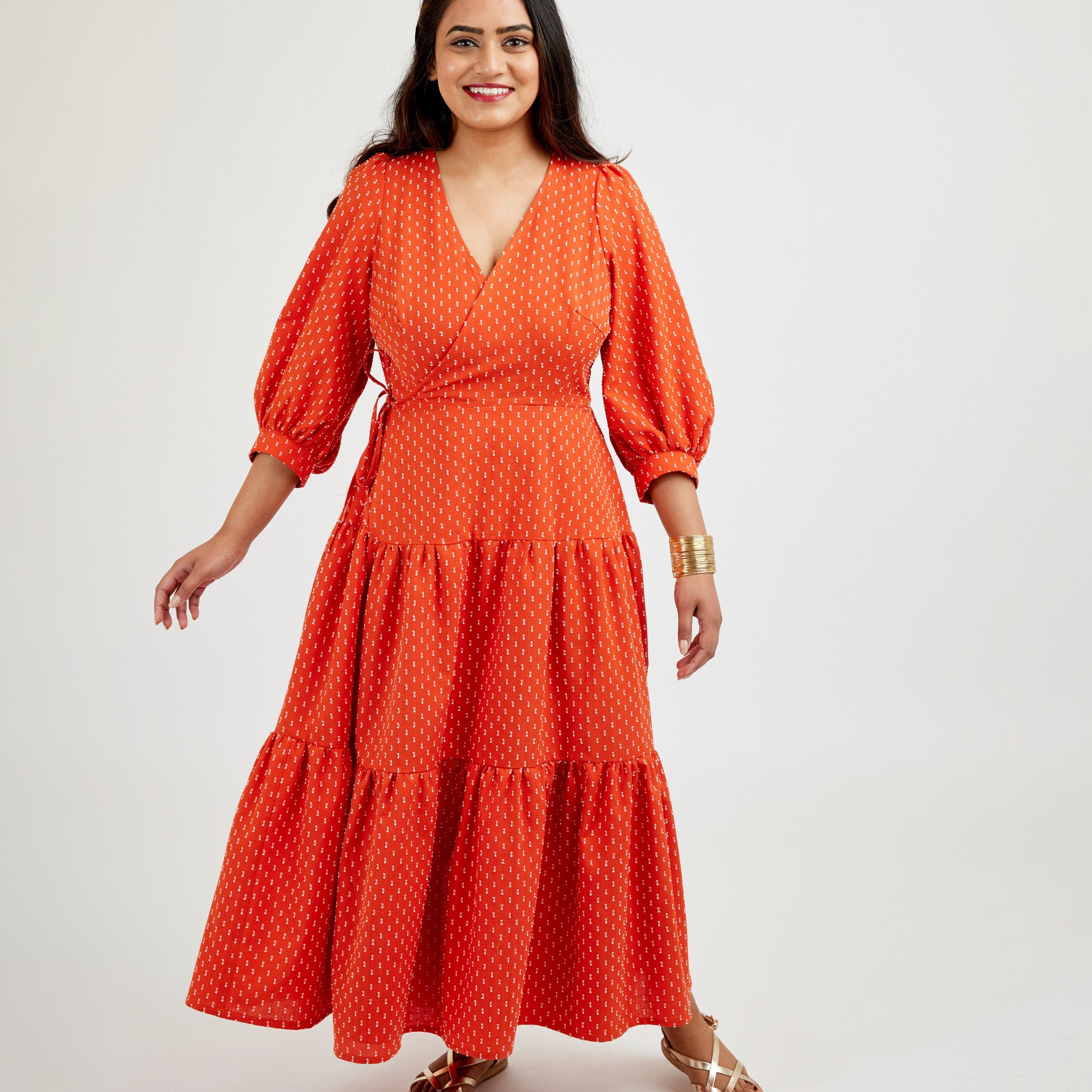 Woman wearing a red dress with a white background. This dress is the Roseclair Wrap Dress sewing pattern from Cashmerette.