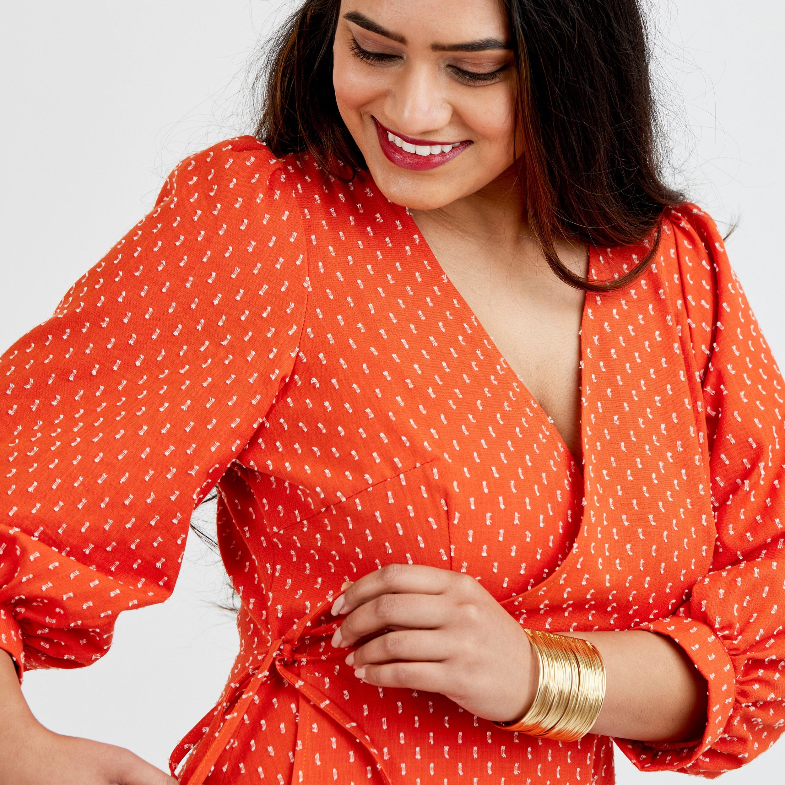 Woman wearing an orange dress with a white pattern on a plain background. This dress is the Roseclair Wrap Dress sewing pattern from Cashmerette.