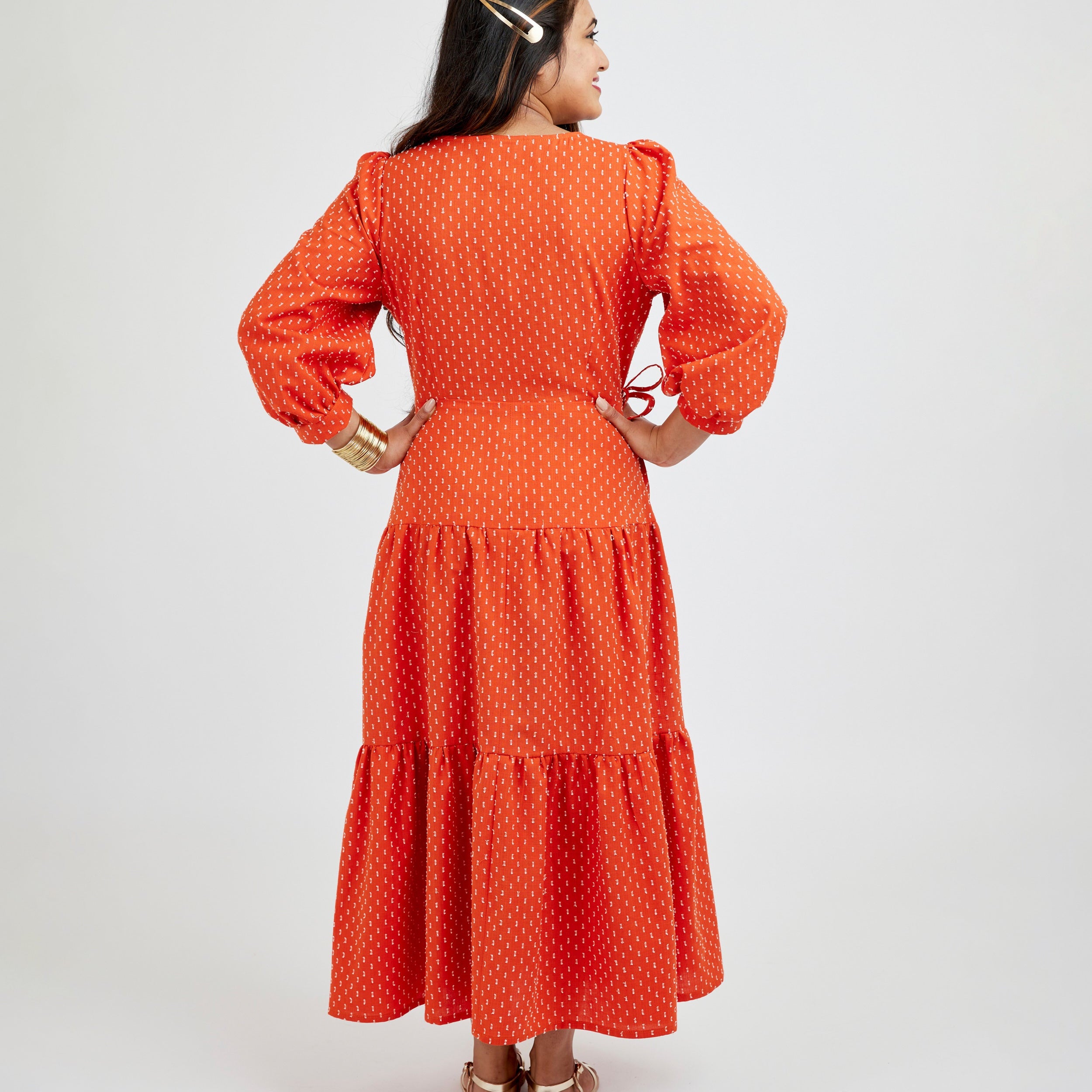 Woman wearing an orange dress with a white background. This dress is the Roseclair Wrap Dress sewing pattern from Cashmerette.