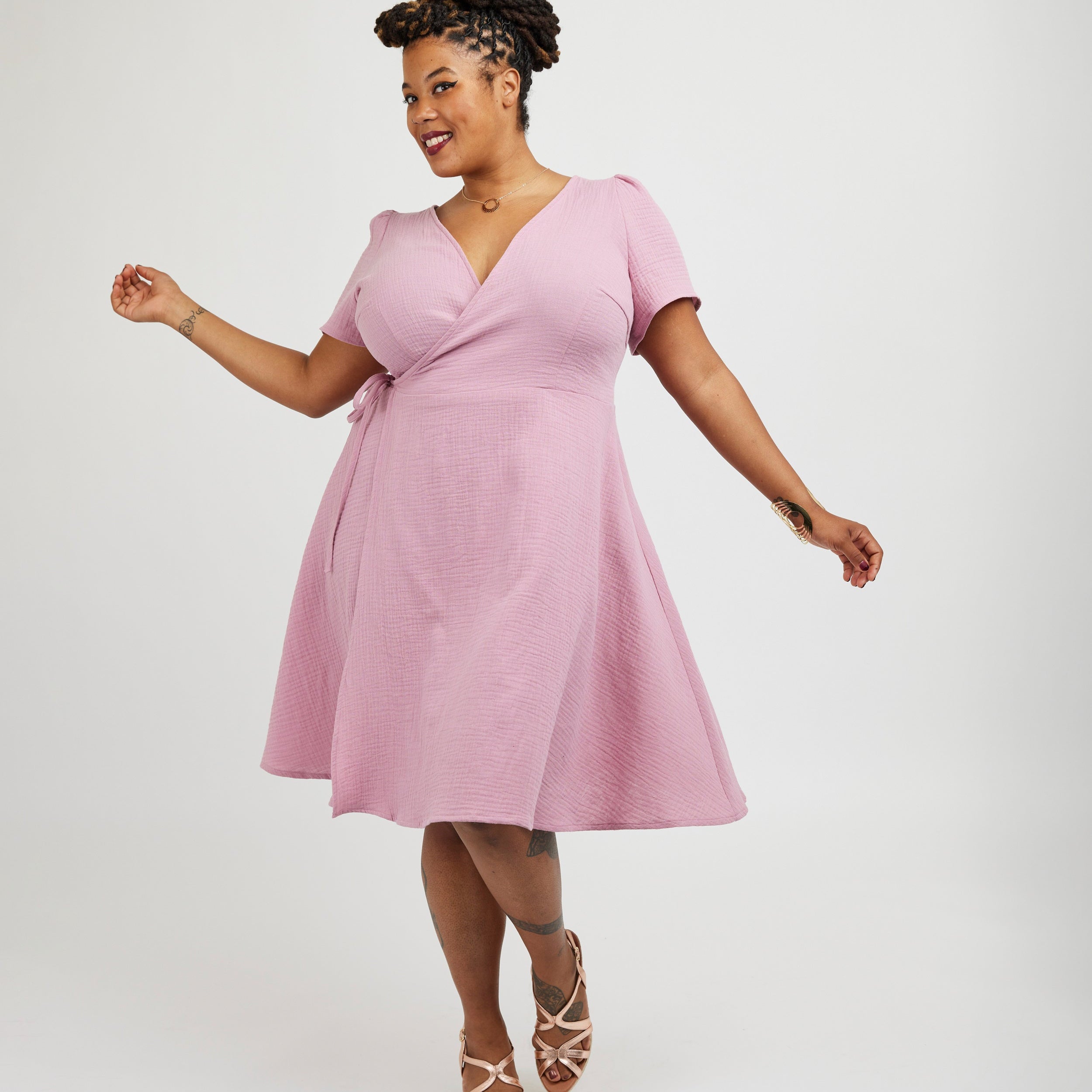 Woman wearing a pink dress on a white background. This dress is the Roseclair Wrap Dress sewing pattern from Cashmerette.